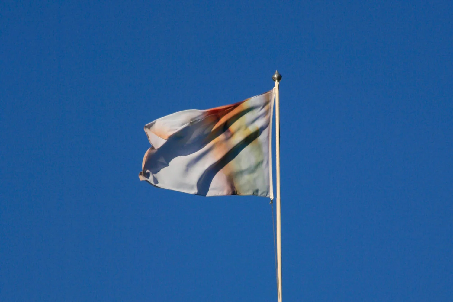 An abstract, colorful flag waving against a clear blue sky.