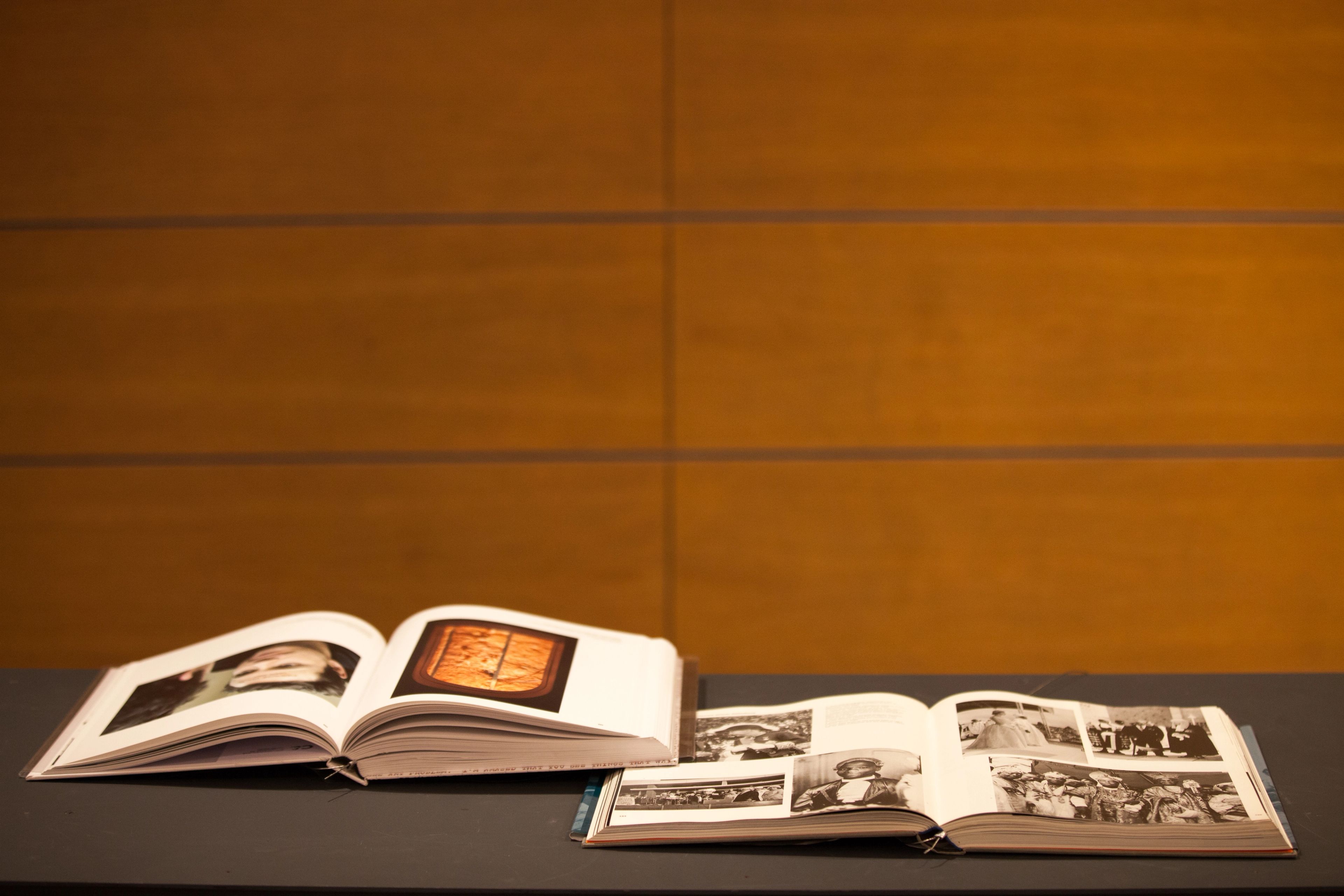 Two open photo albums, one showing color images and the other black and white photos, on a dark surface against a wooden wall.