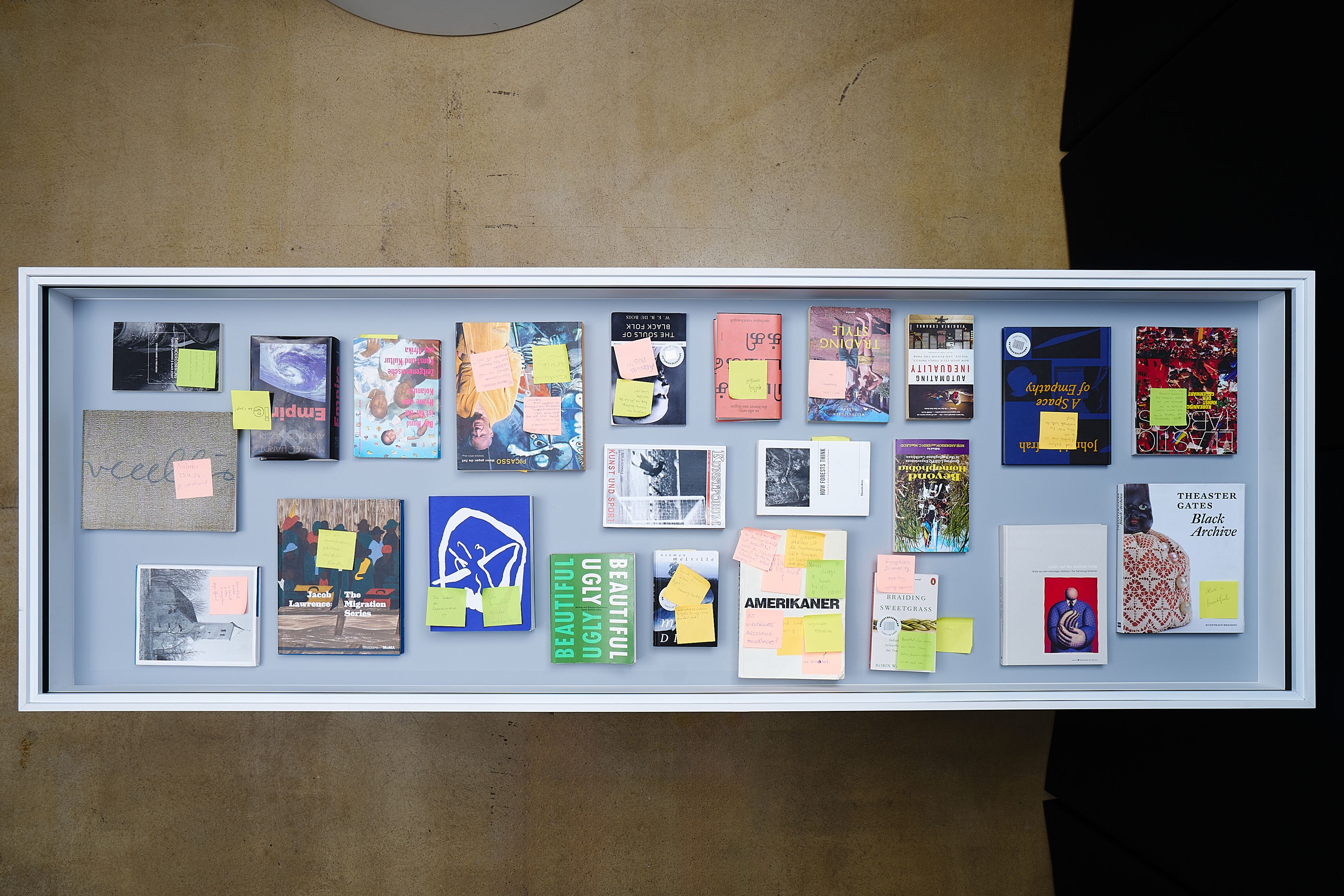 Books and postcards with sticky notes displayed in a white framed case.