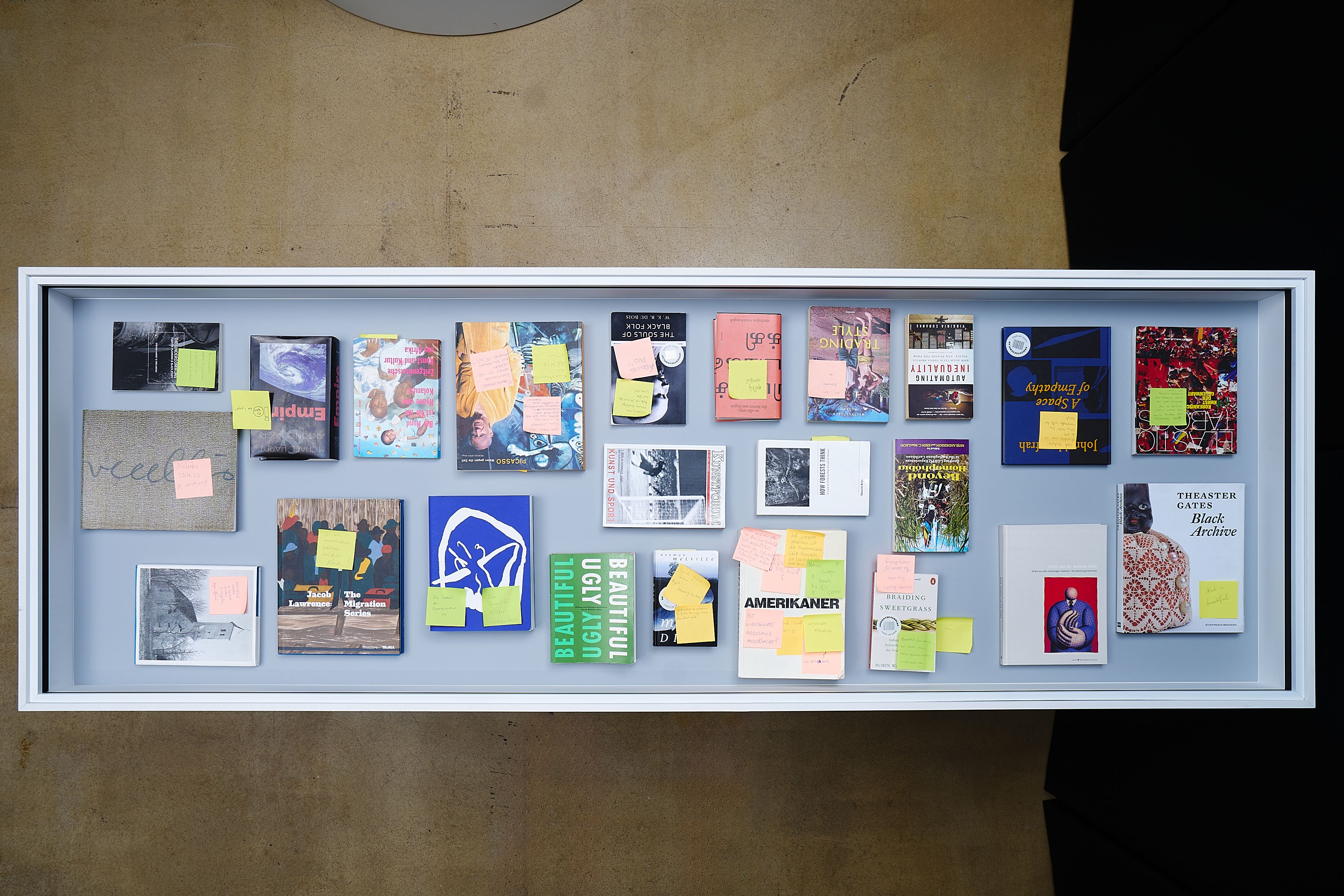 Books and postcards with sticky notes displayed in a white framed case.