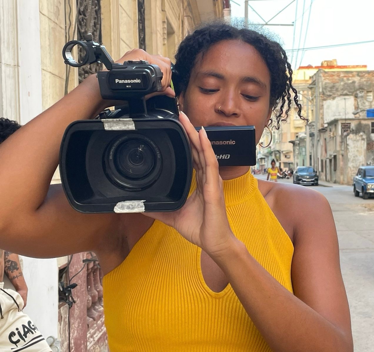 A woman in a yellow top operates a video camera on a city street.
