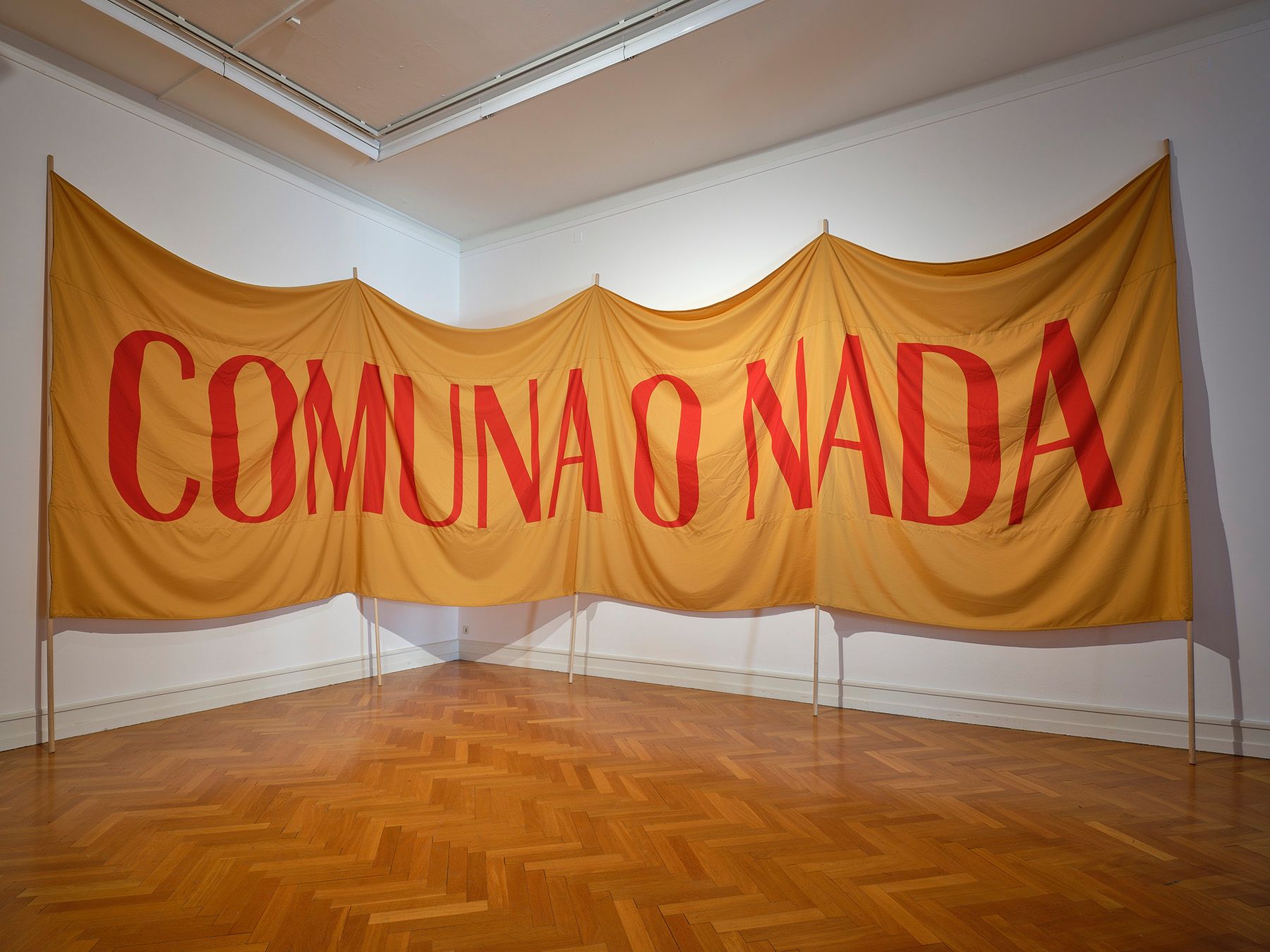 A large golden-yellow banner with red text "COMUNA O NADA" displayed in an art gallery.