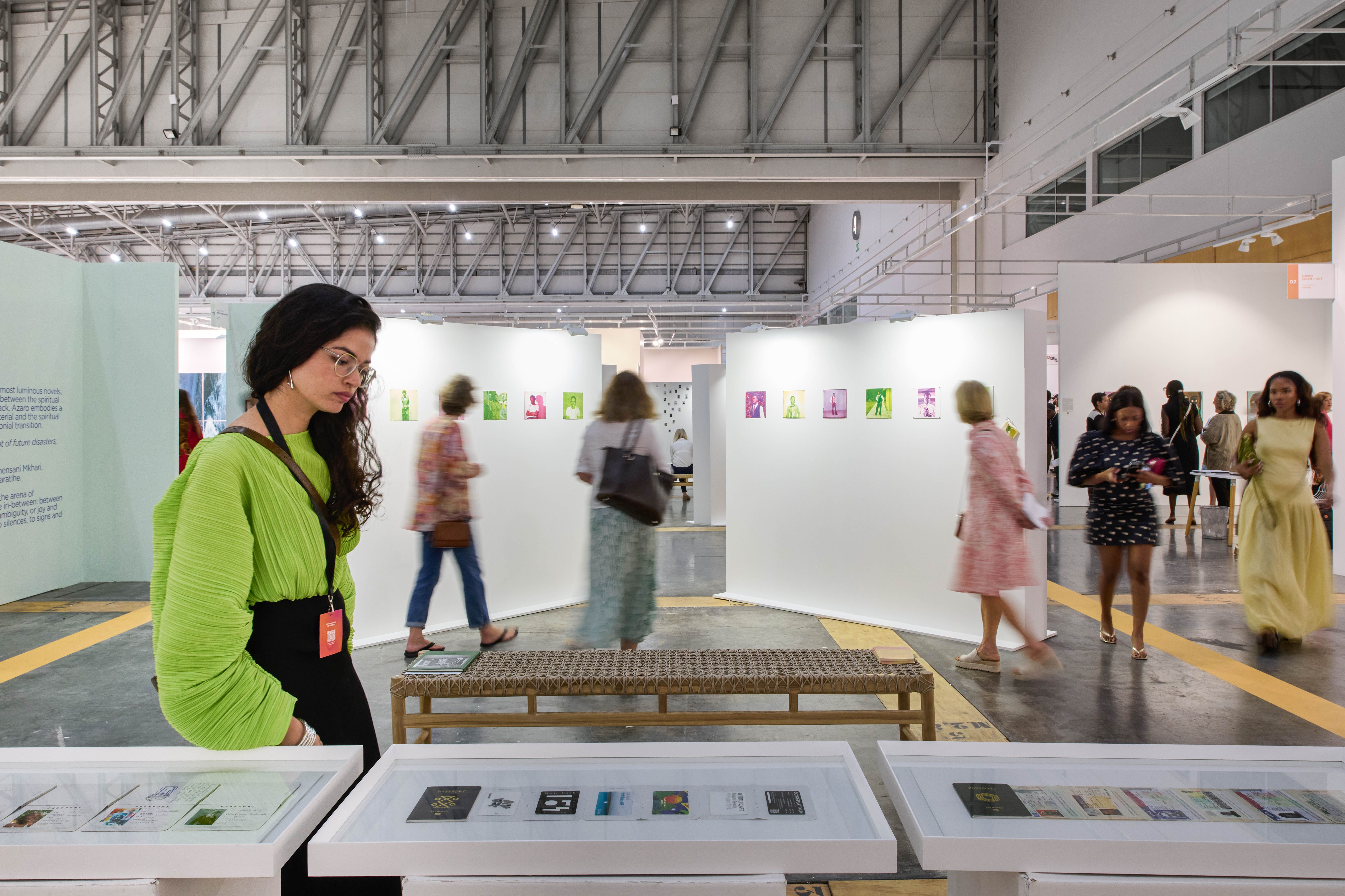 A woman in a bright green top examines items in display cases at a busy art exhibition.