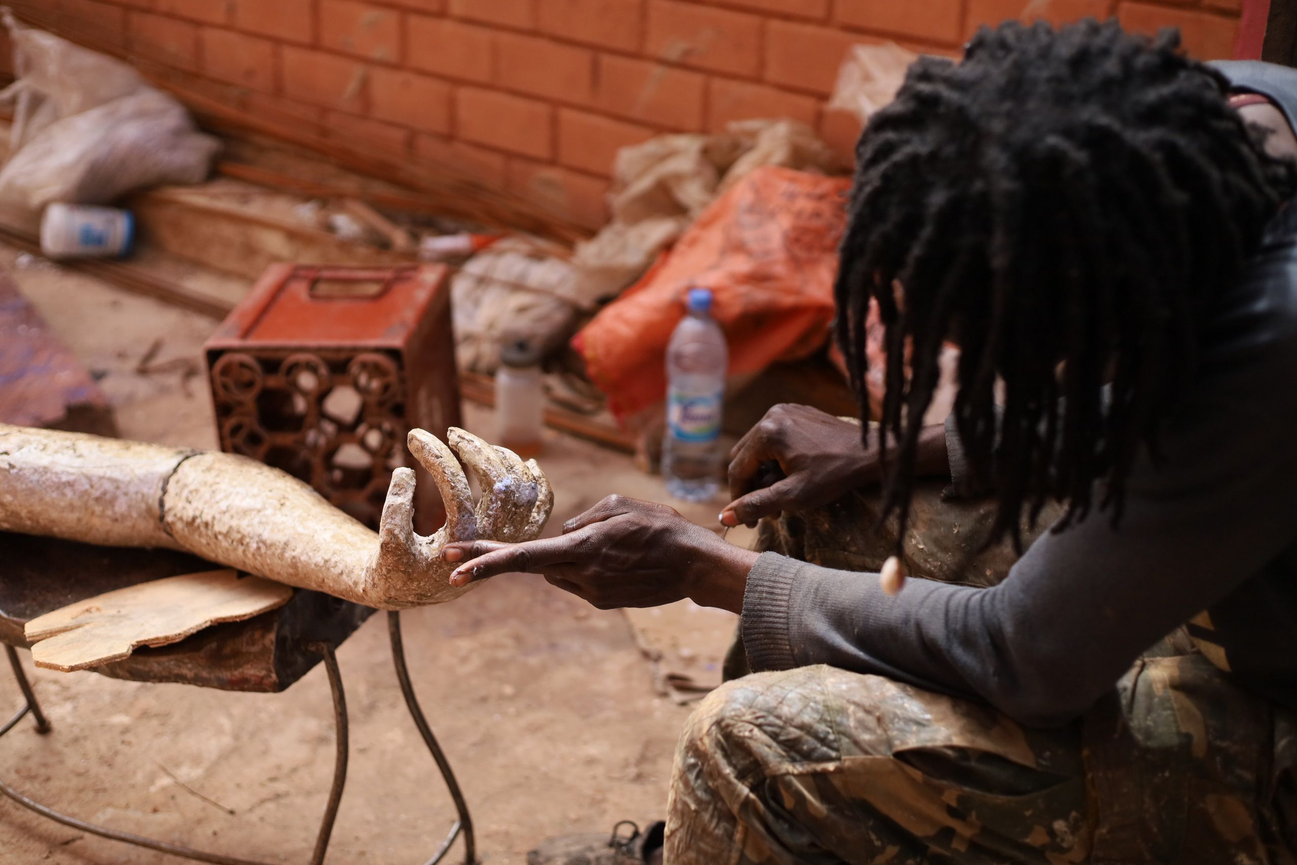 A person with dreadlocks works on a textured arm and hand sculpture.