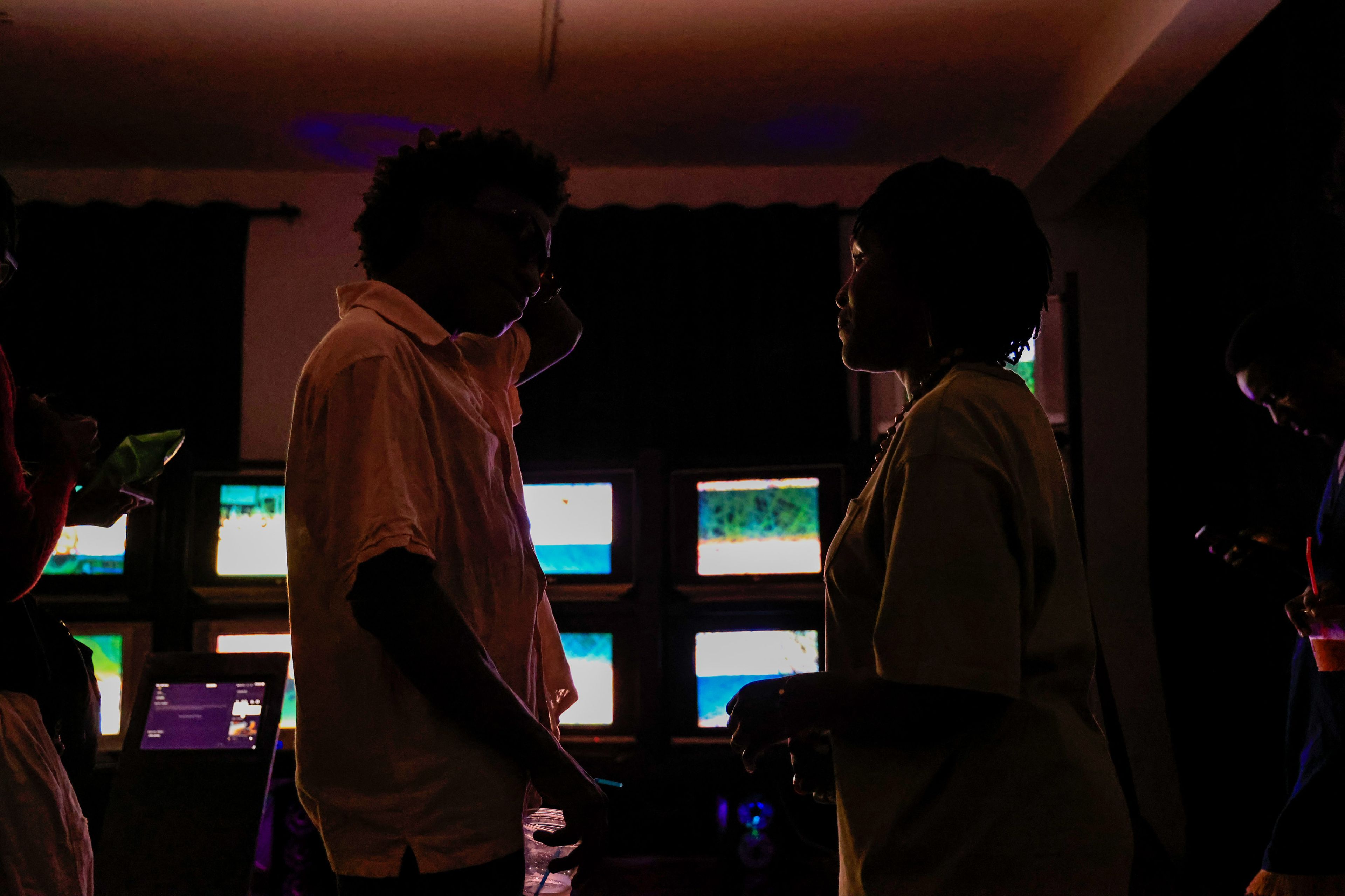 Two people in silhouette stand in a dark room illuminated by several glowing screens.