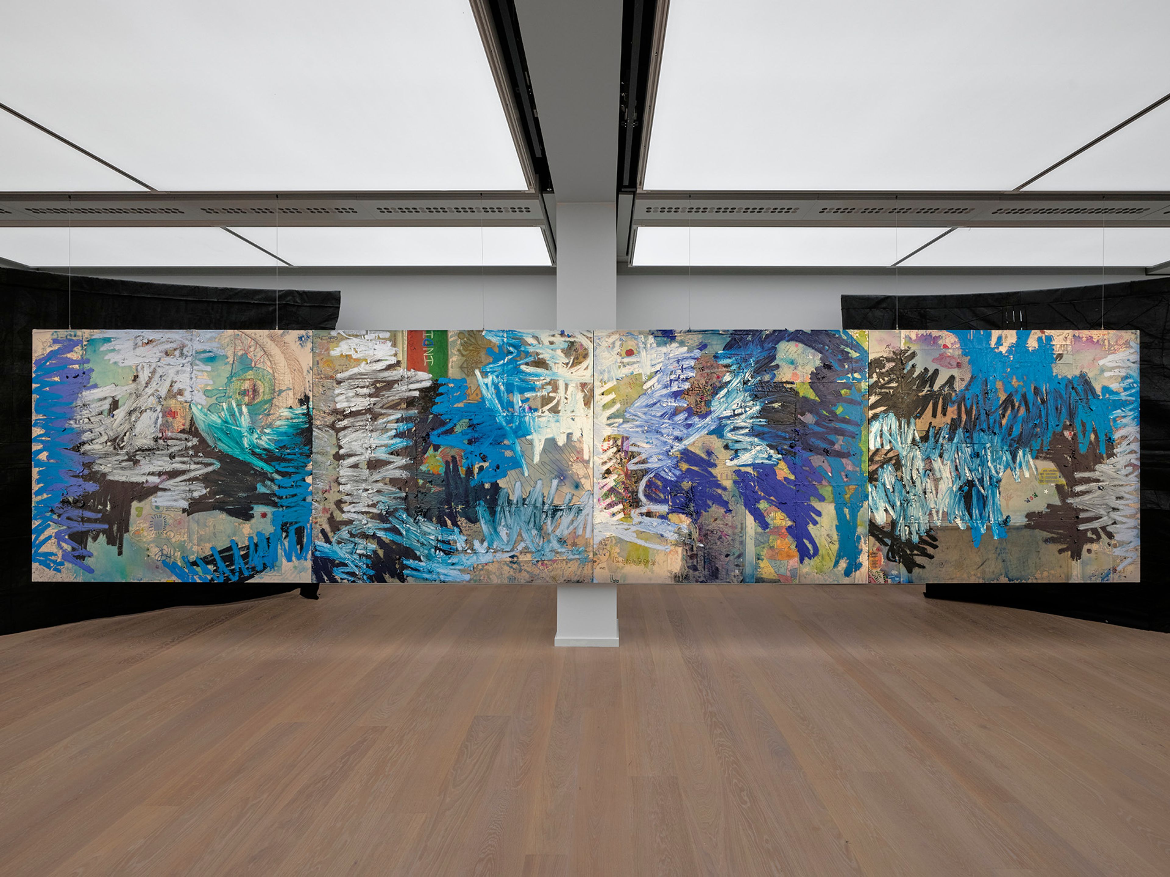 A multi-panel abstract painting with energetic blue, white, and purple marks, displayed in a modern gallery.