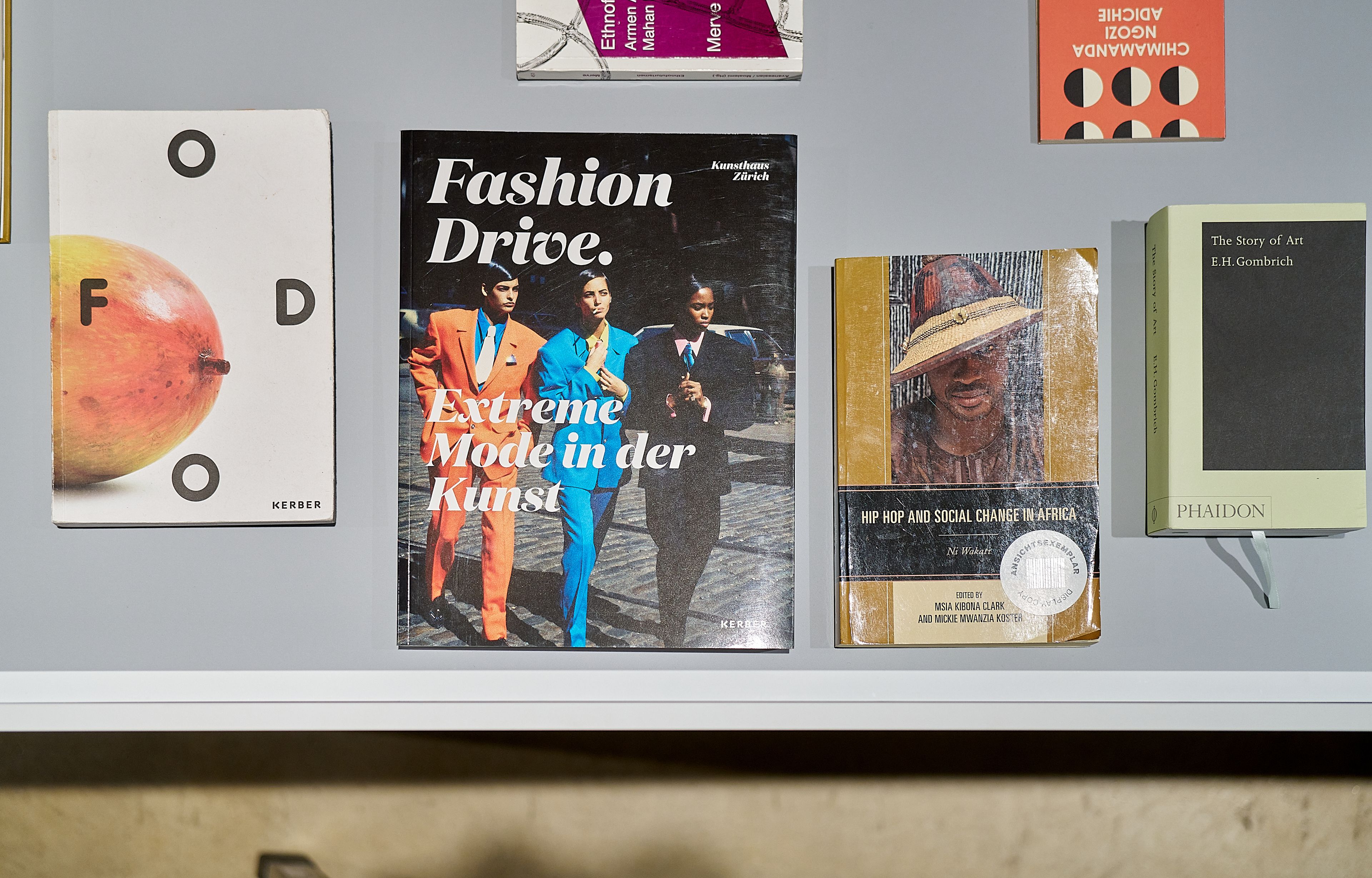 A shelf displays several books including "Fashion Drive," "Hip Hop and Social Change in Africa," and "The Story of Art."