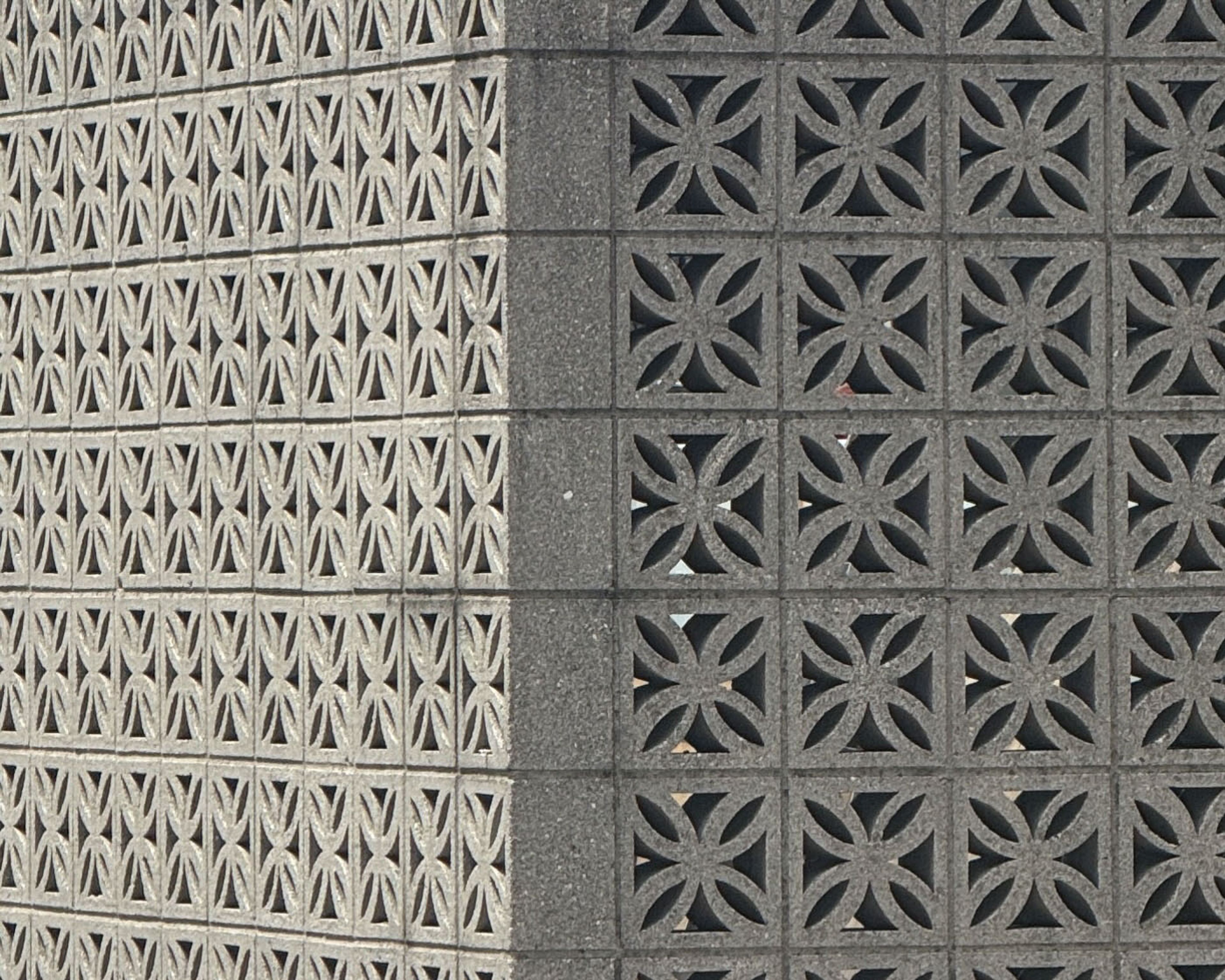 Corner of a decorative concrete block wall featuring two distinct geometric patterns: light grey hourglass shapes on the left, and dark grey four-petal flower shapes on the right.