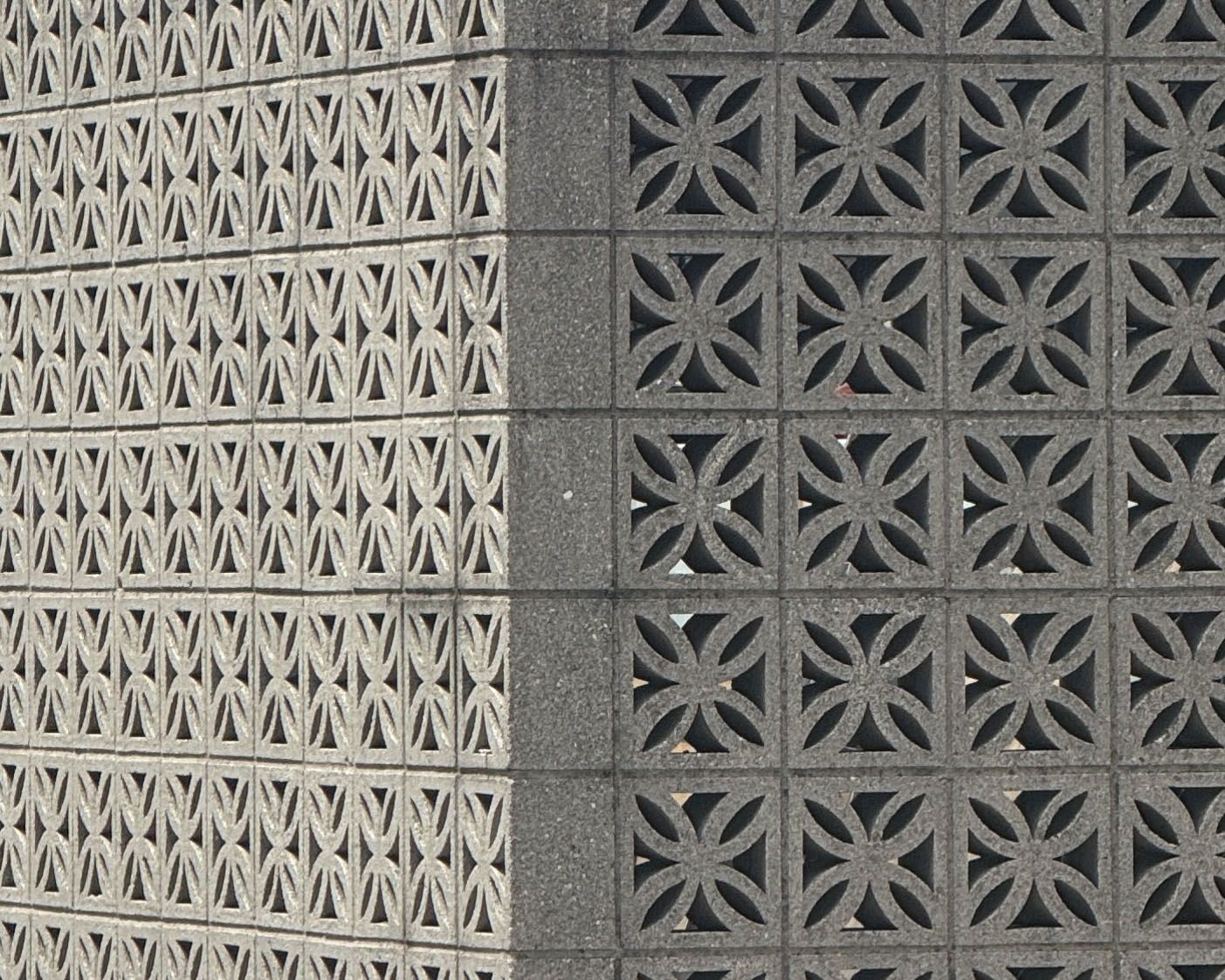 Corner of a decorative concrete block wall featuring two distinct geometric patterns: light grey hourglass shapes on the left, and dark grey four-petal flower shapes on the right.