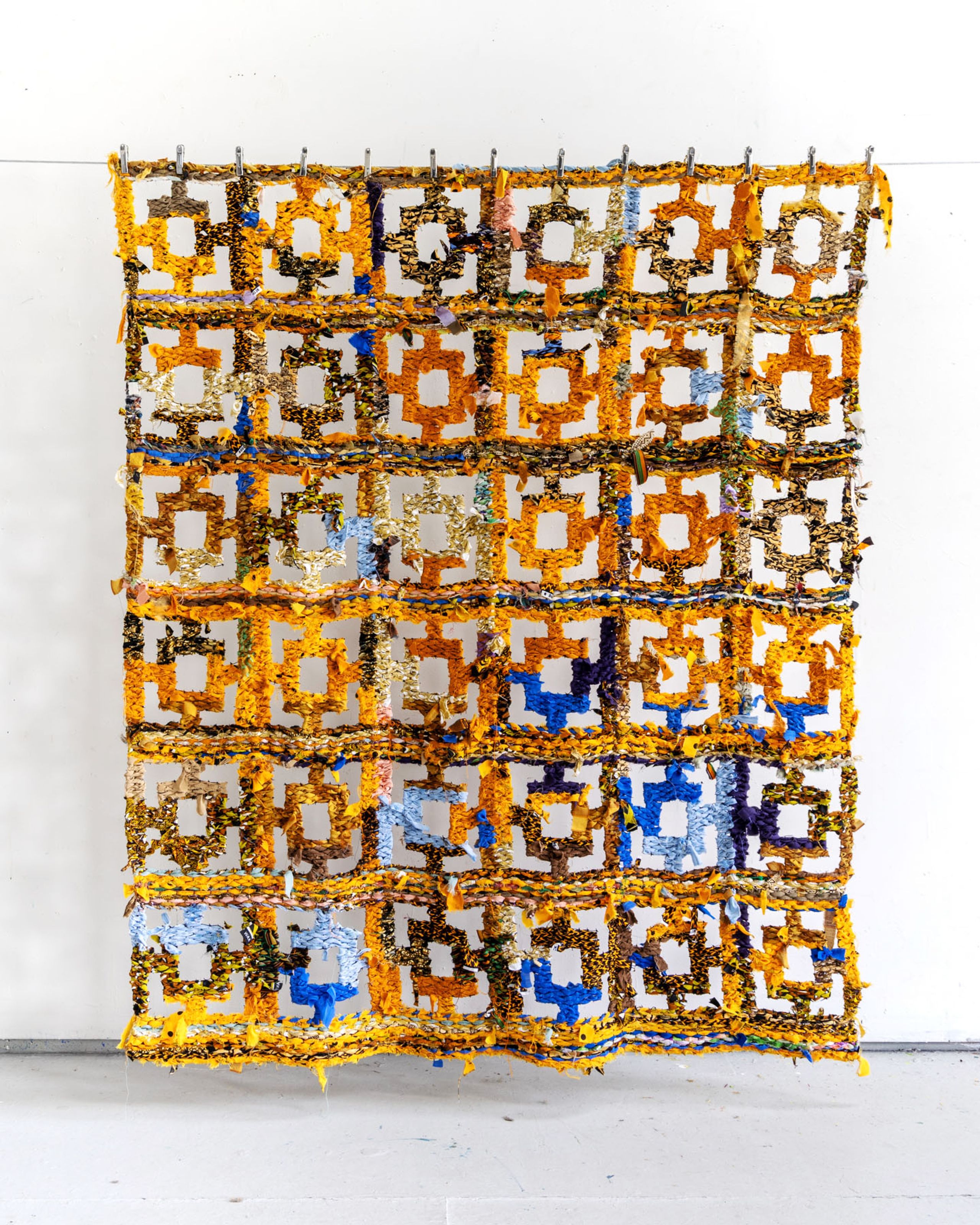 Textured woven art piece with yellow, orange, and blue geometric patterns.