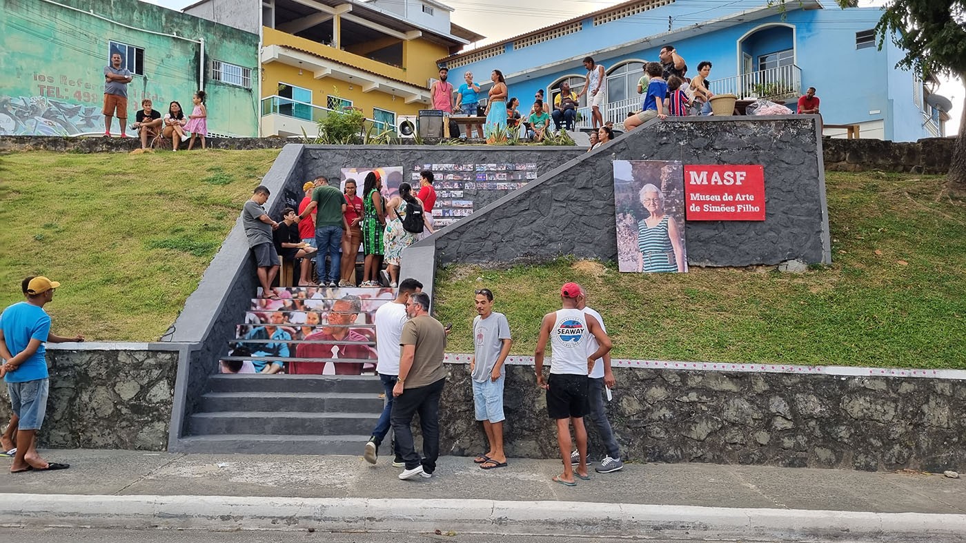 A public staircase with a mural of faces on the risers, surrounded by people, and a MASF sign on the right.