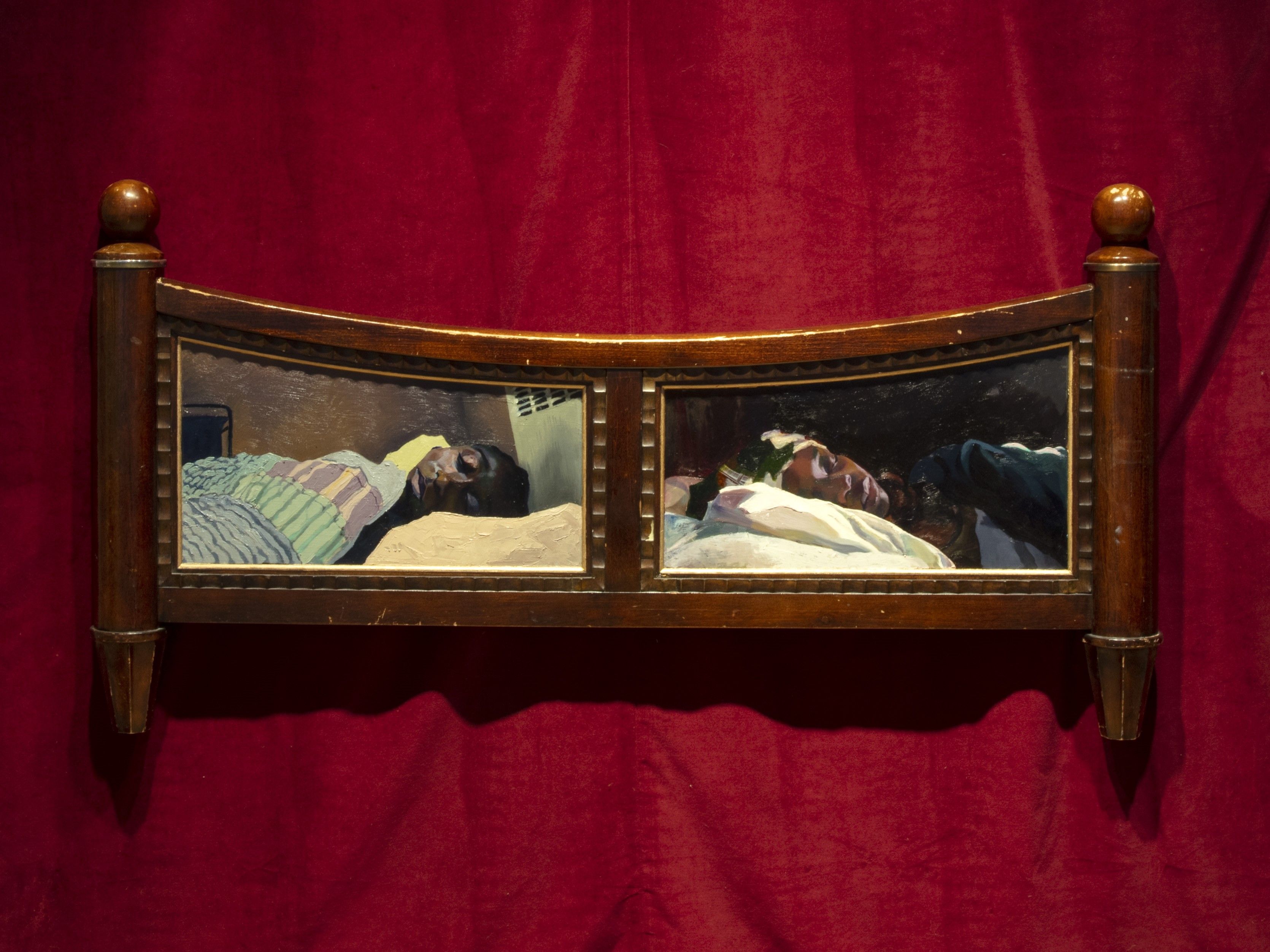A carved wooden headboard featuring two paintings of individuals lying in bed, set against a deep red draped background.