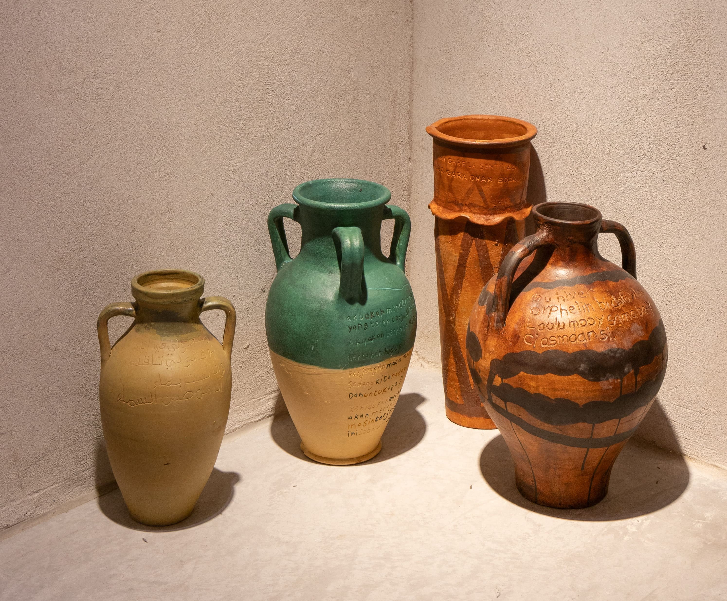 Four ceramic vases of varying shapes and colors, some inscribed with text or patterns, displayed in a corner.
