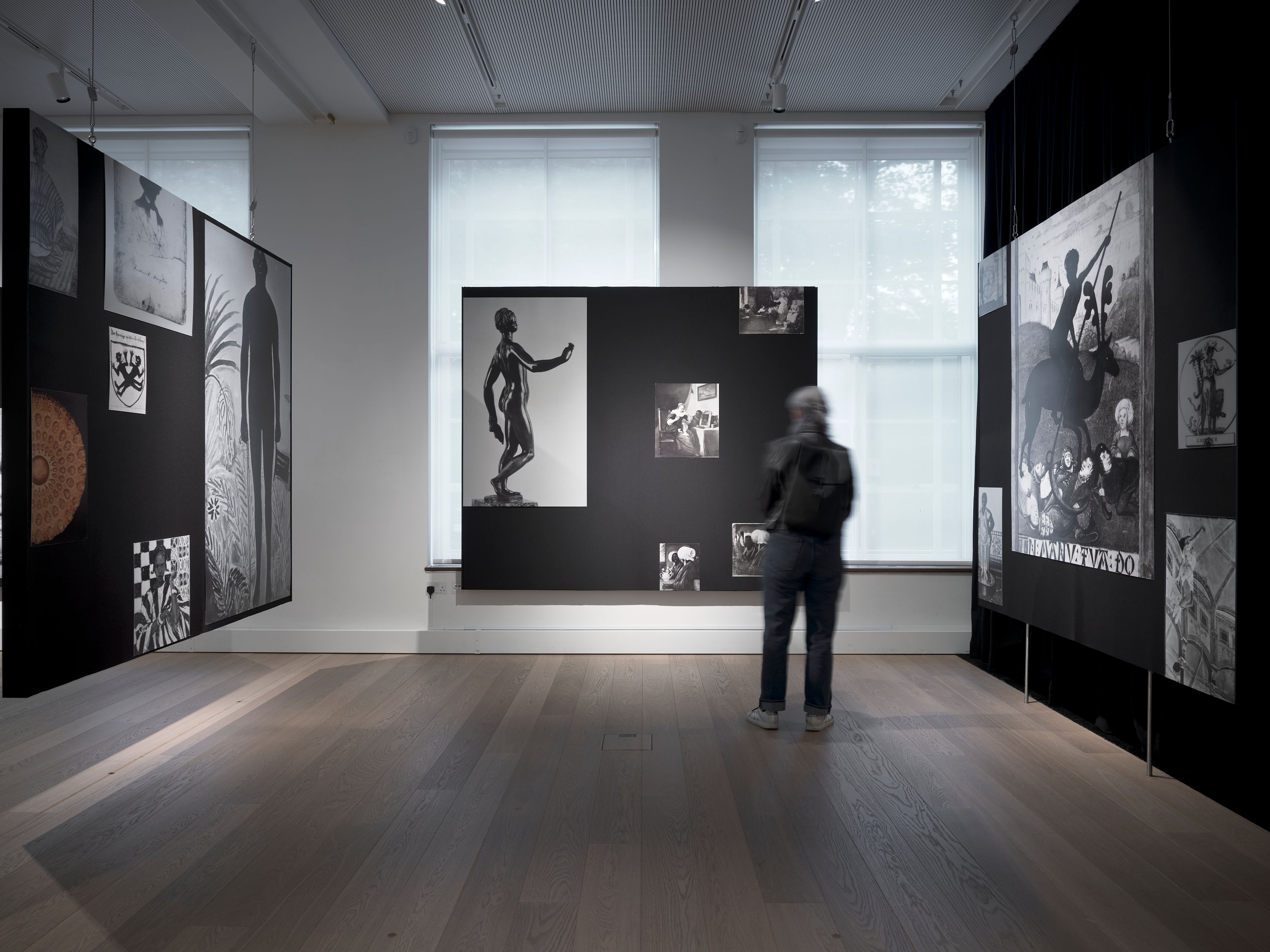 A person views black and white art displayed on large dark panels in a gallery.