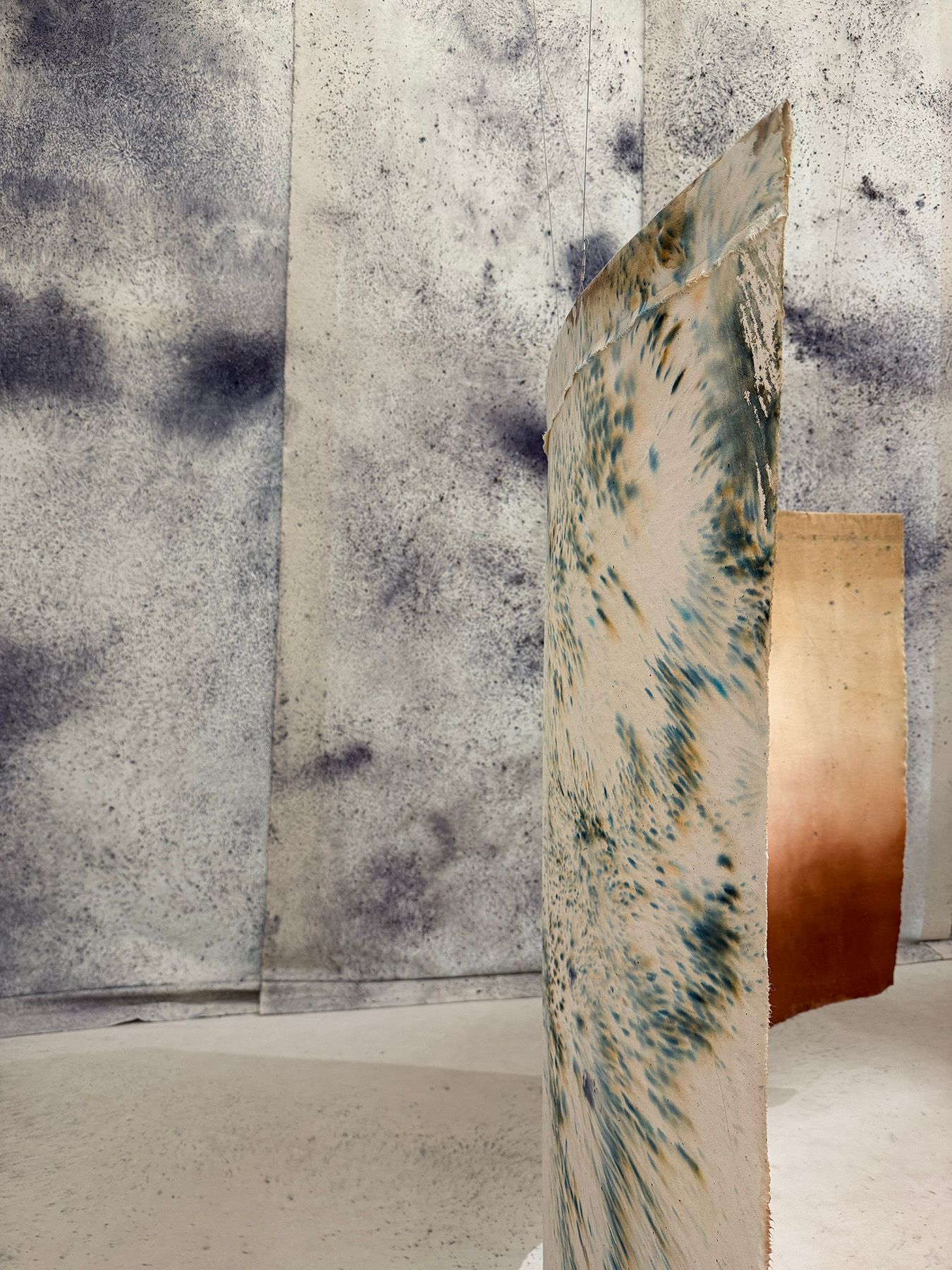 A curved panel with blue and brown splatters stands in front of mottled gray and gradient brown textured panels.