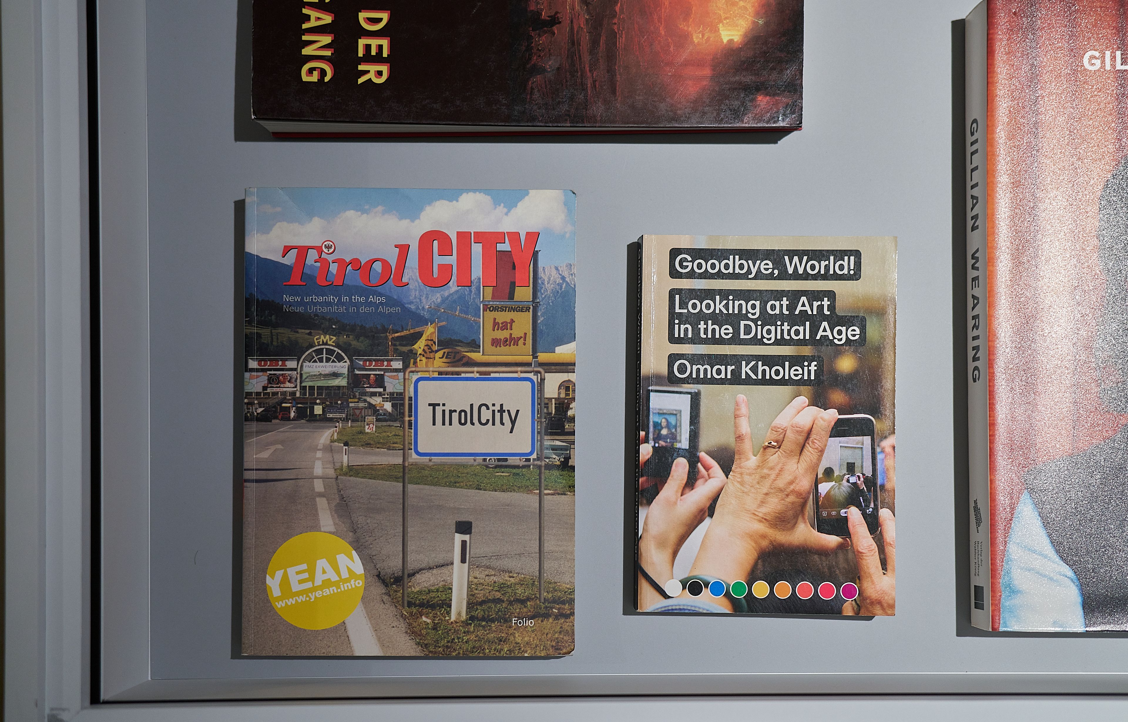 Two books are displayed: "Tirol CITY" with a road sign and mountains, and "Goodbye, World! Looking at Art in the Digital Age" showing hands with smartphones.