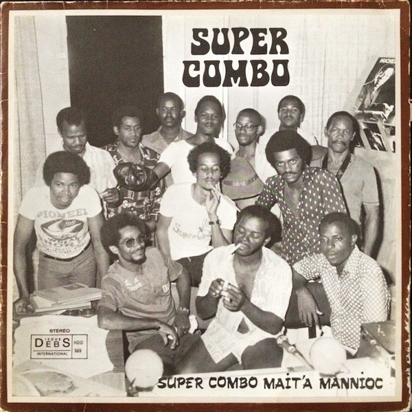 Black and white album cover for Super Combo's "Mait'a Mannioc", showing a large group of men in a relaxed pose, with some smoking.