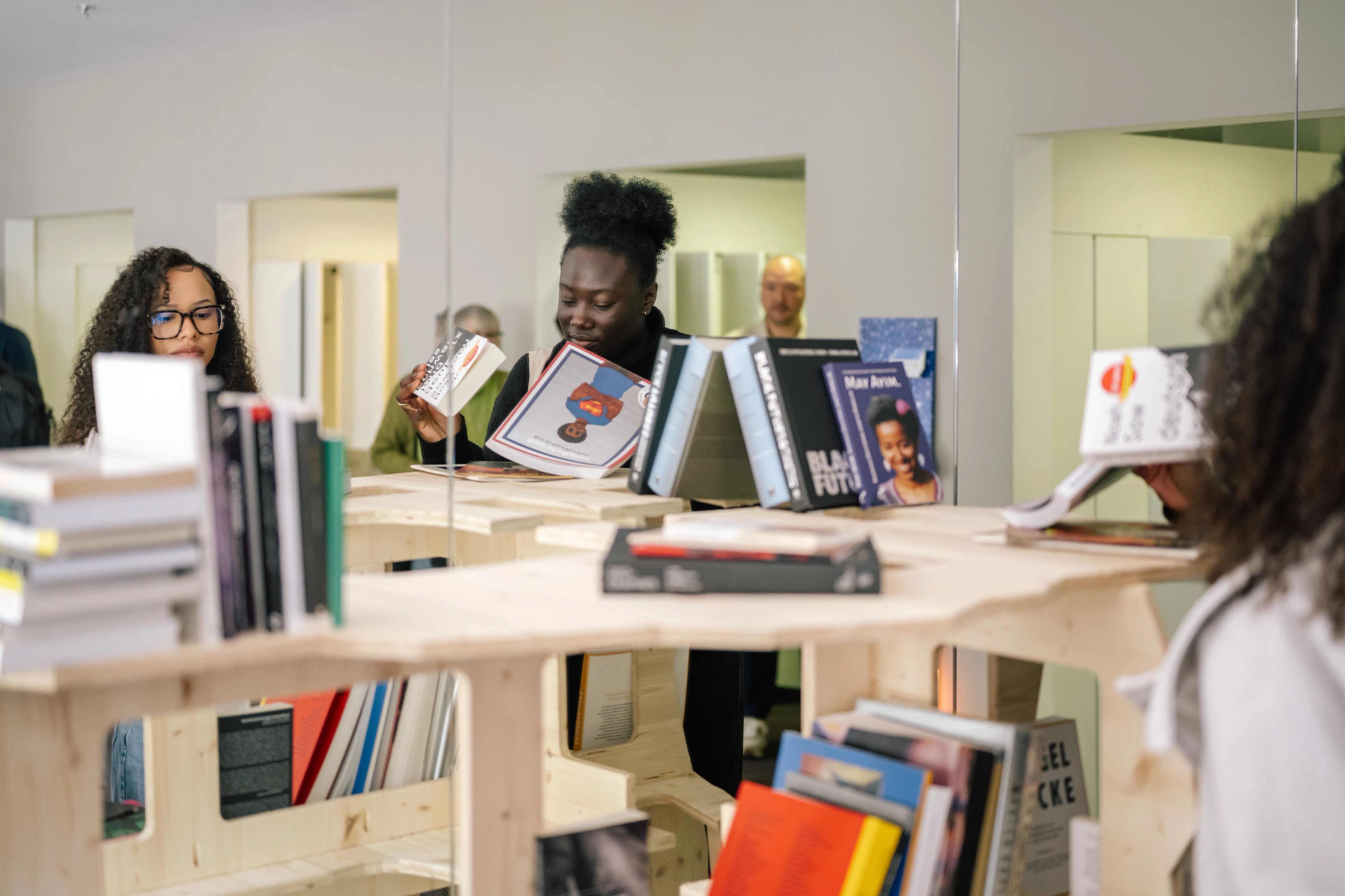 Two women browse books on light wooden shelves, one smiling as she holds an open book.