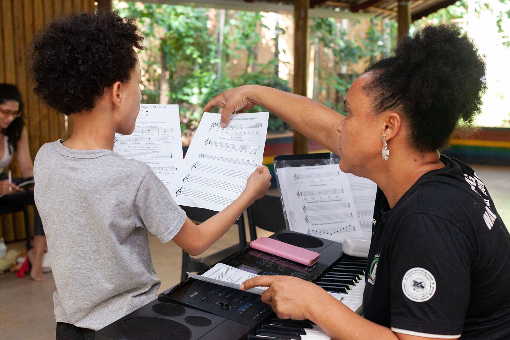 A woman teaches a young student to play an electronic keyboard, pointing to sheet music.