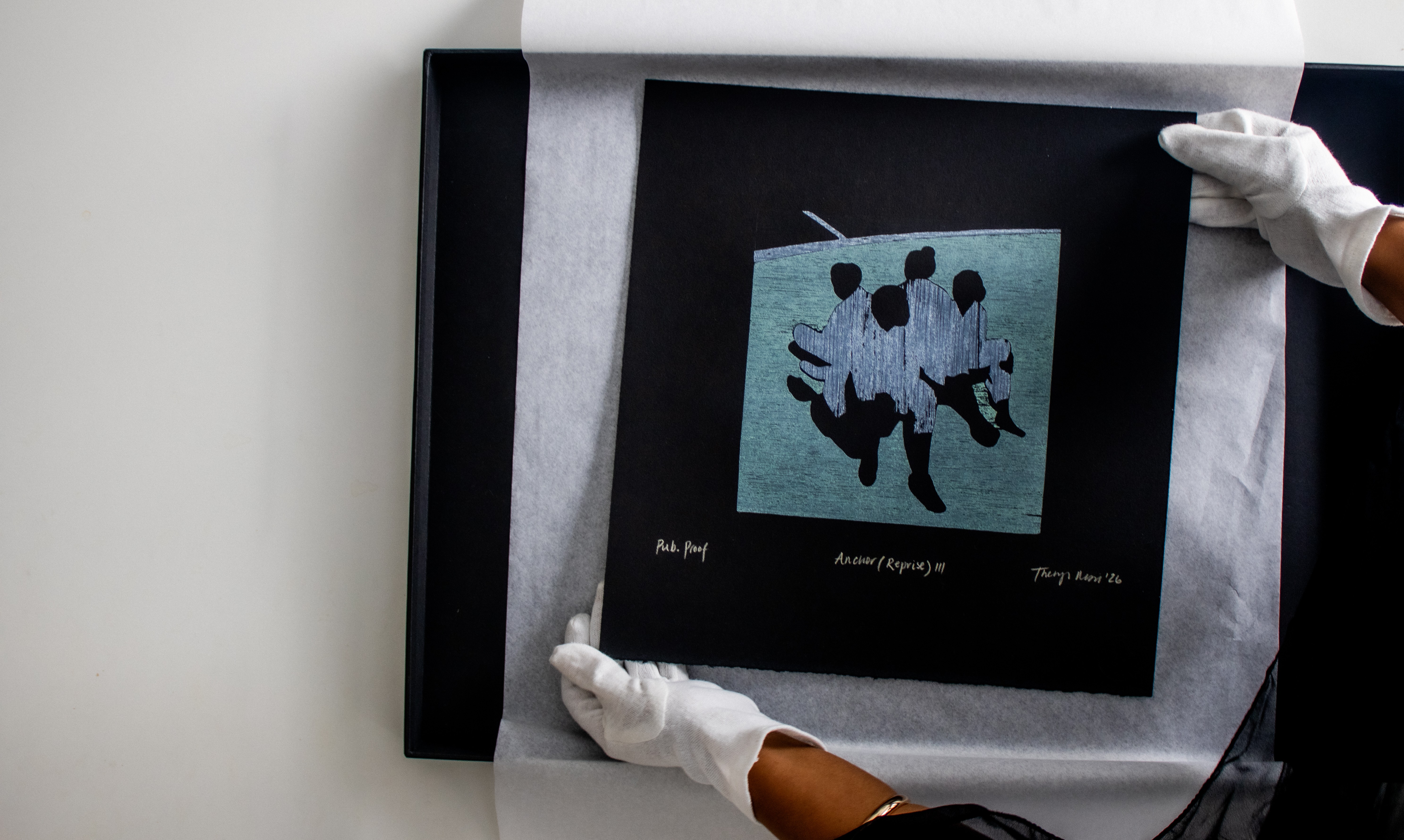 A person in white gloves places a black print depicting four abstract blue and black figures into a black frame.