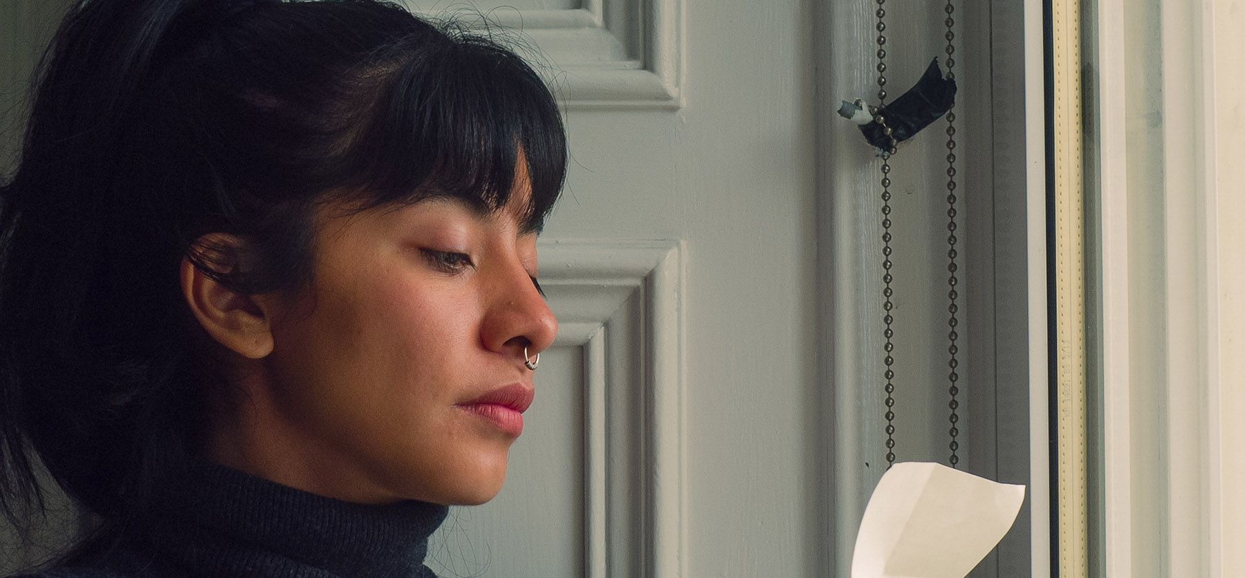 Woman with dark hair and a nose ring looking down in profile.