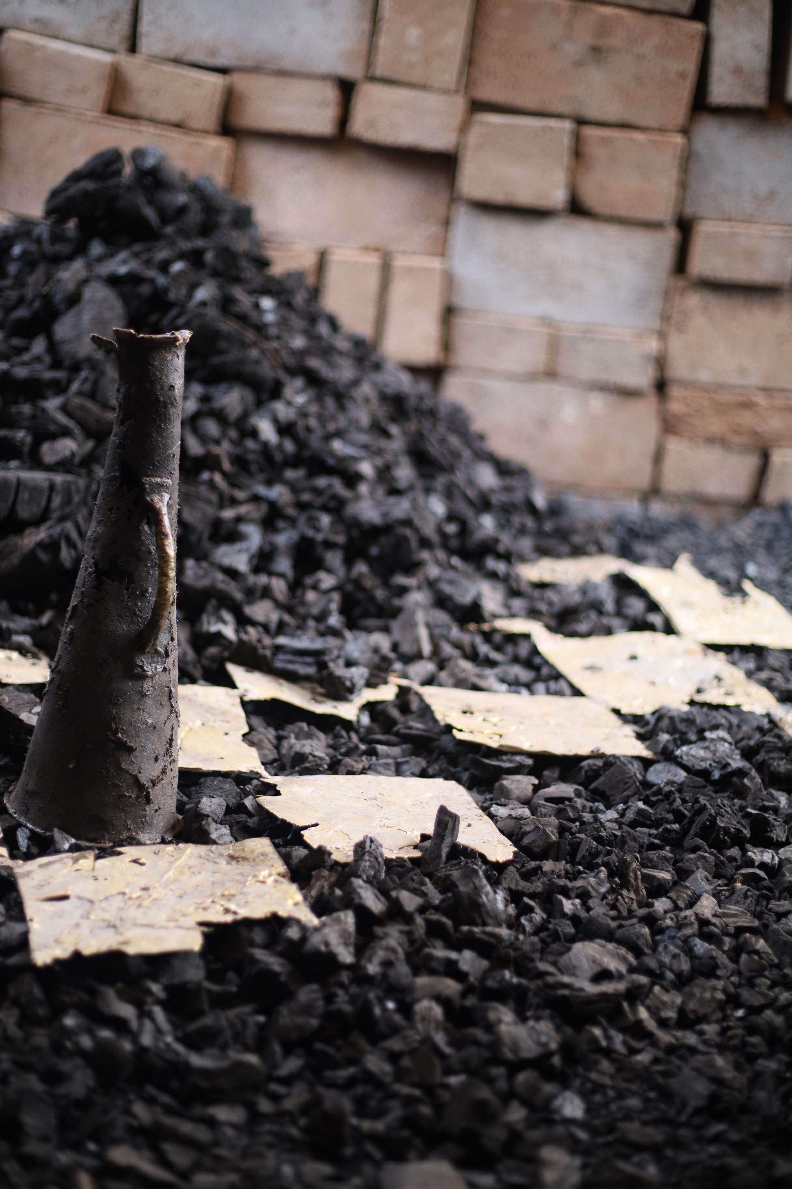 A dark conical object stands upright in a pile of charcoal and light fragments, with a brick wall in the background.