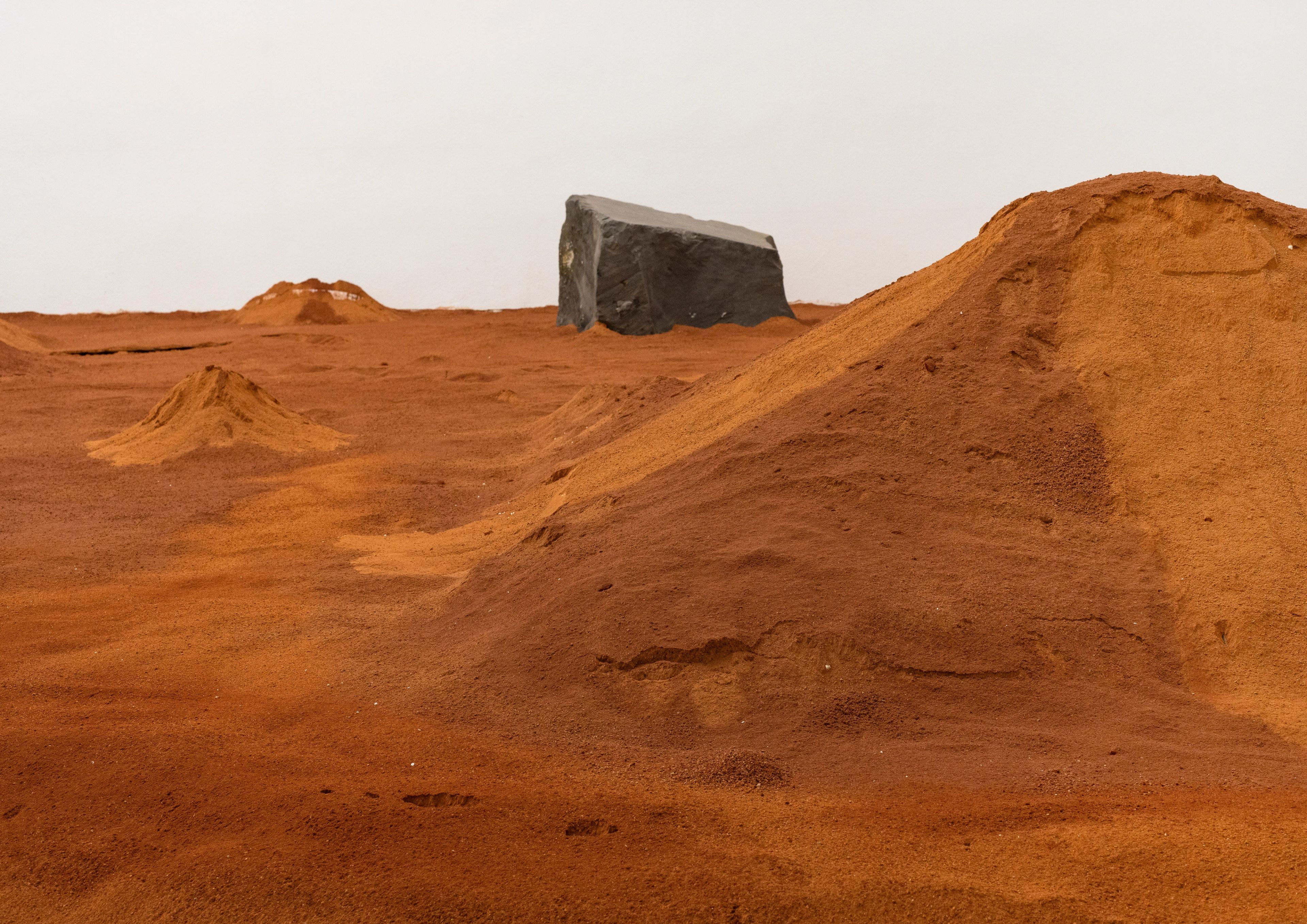 A reddish-brown sandy landscape with small mounds and a large dark grey block in the distance.