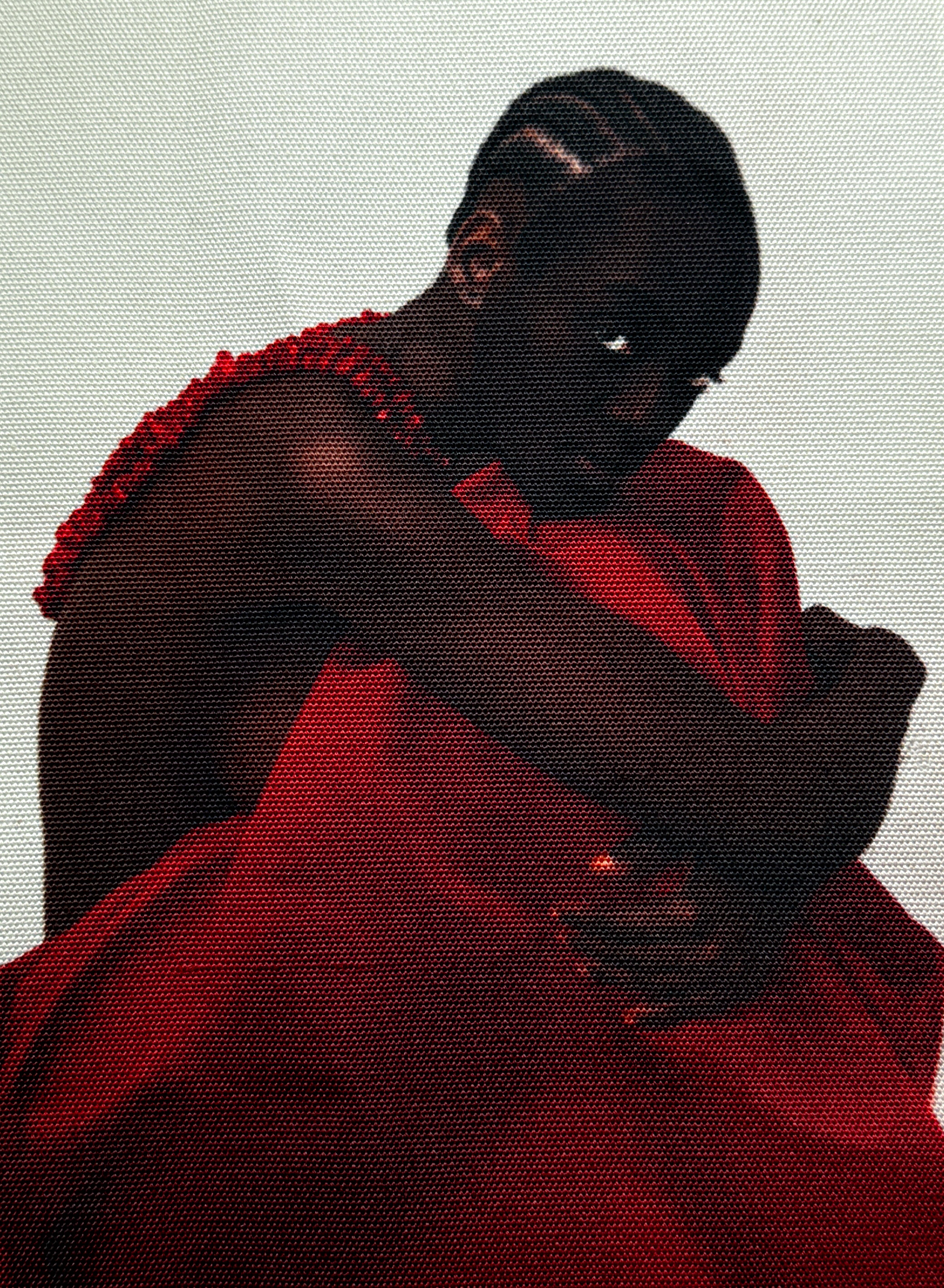 A dark-skinned person in a ruffled red top and draped red fabric, huddled with one eye peering from shadow.