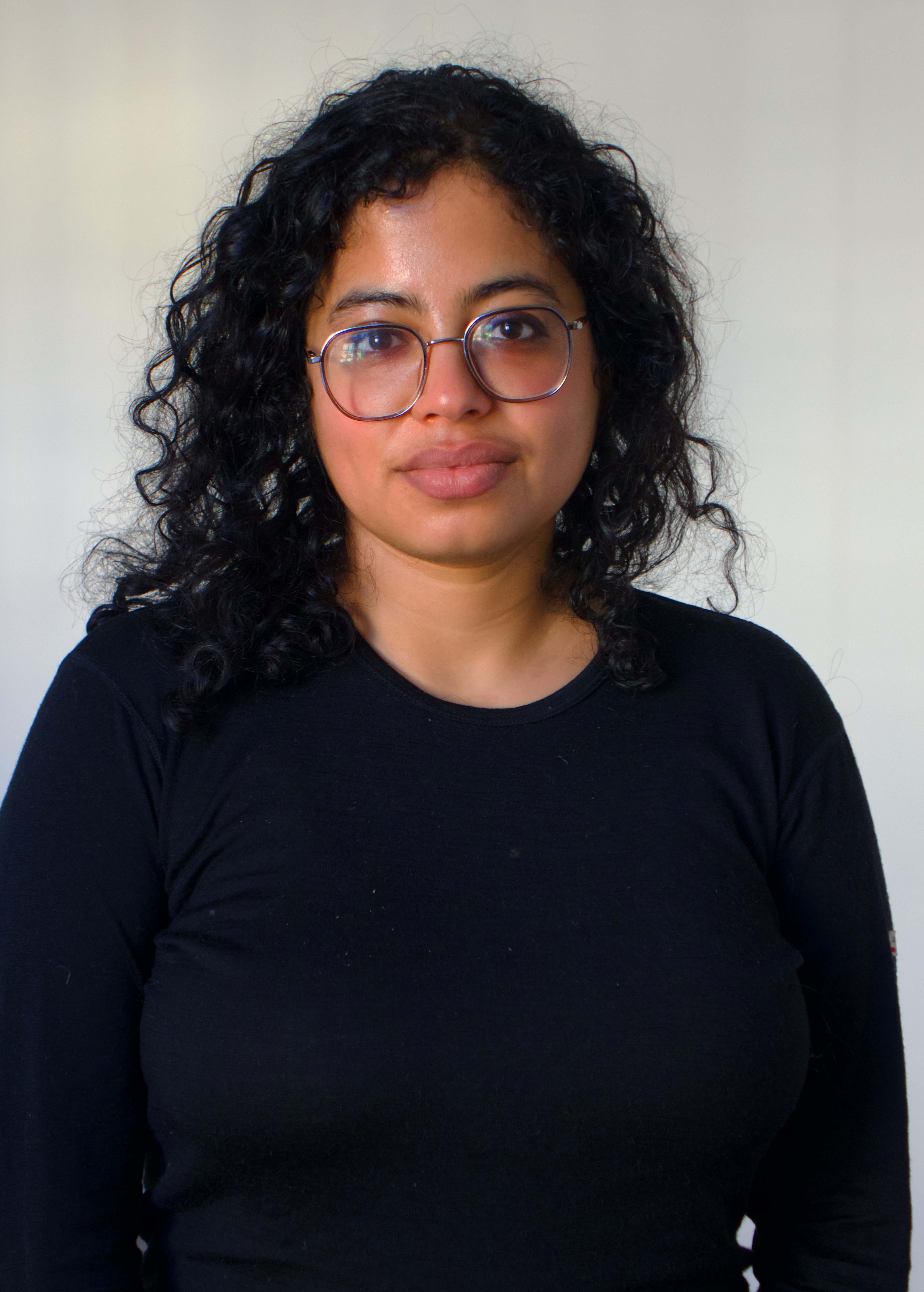 Headshot of a woman with dark curly hair and glasses, wearing a black long-sleeved shirt.