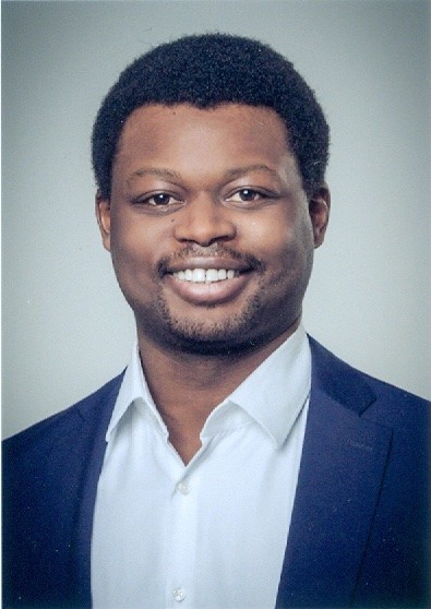 Headshot of a smiling Black man with short dark curly hair and a beard, wearing a white shirt and a dark blue jacket.