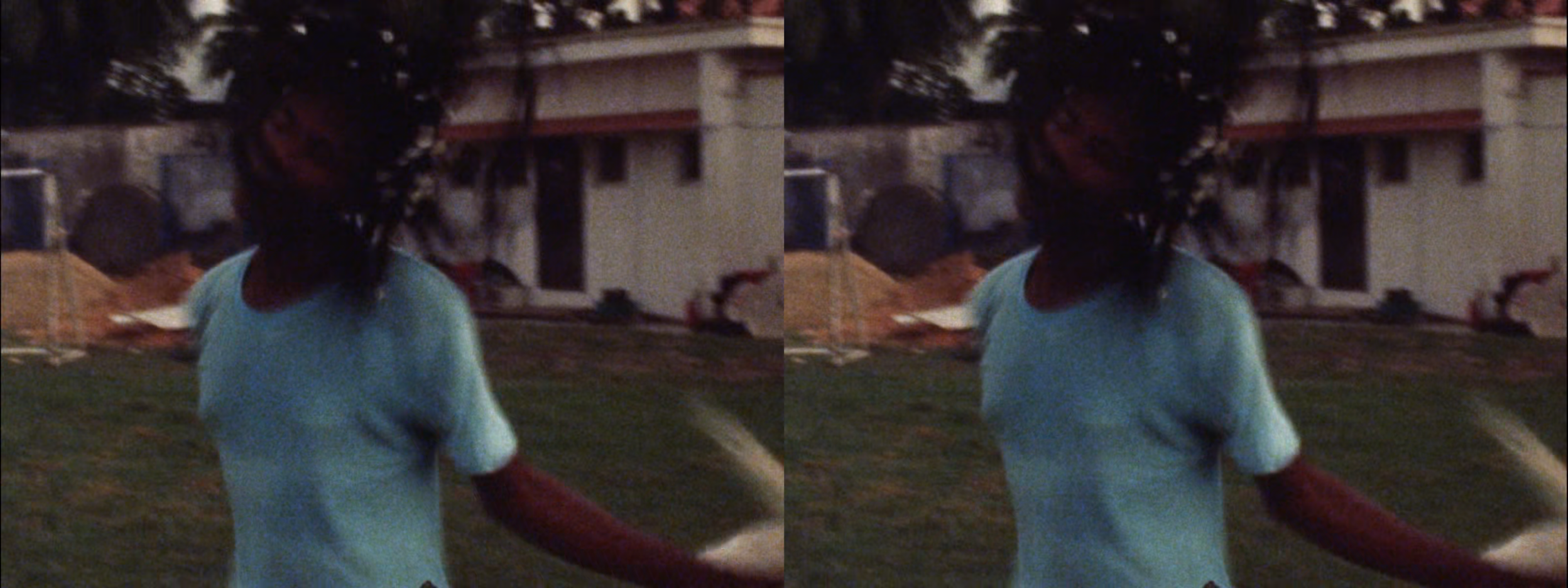 Two identical, blurry film stills show a person in a light blue t-shirt with outstretched arms on a grassy lawn, with a building in the background.
