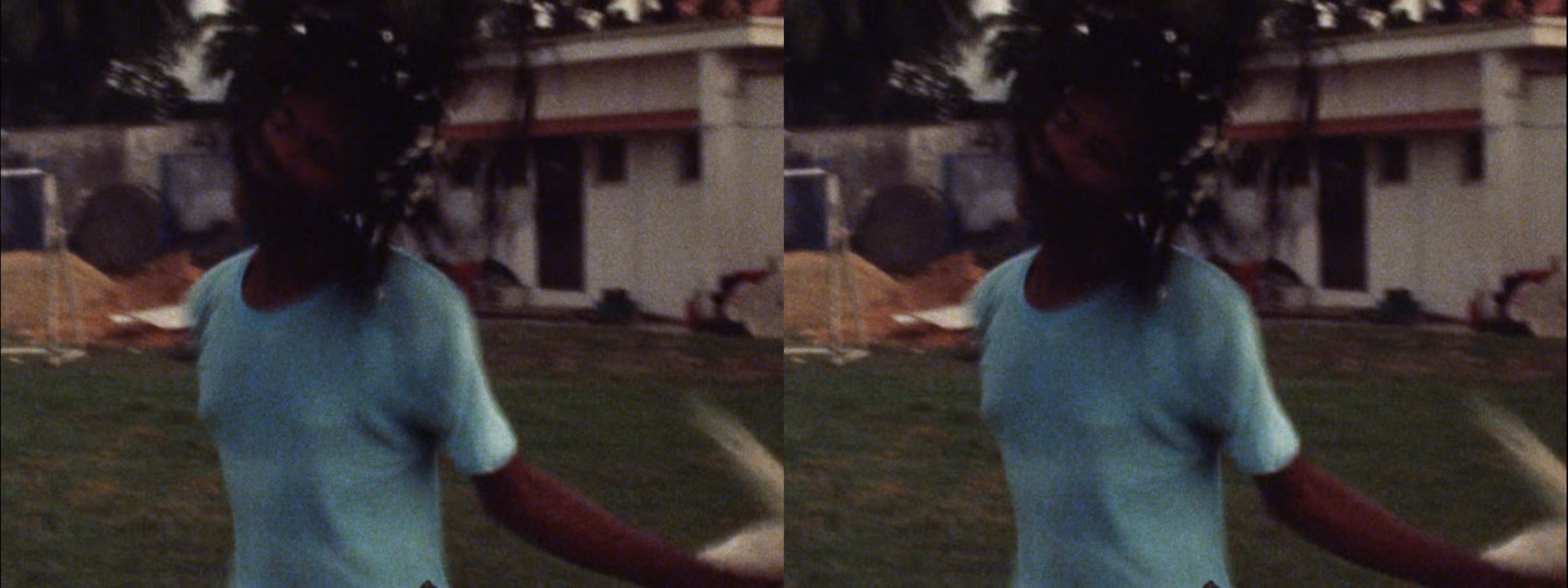 Two identical, blurry film stills show a person in a light blue t-shirt with outstretched arms on a grassy lawn, with a building in the background.