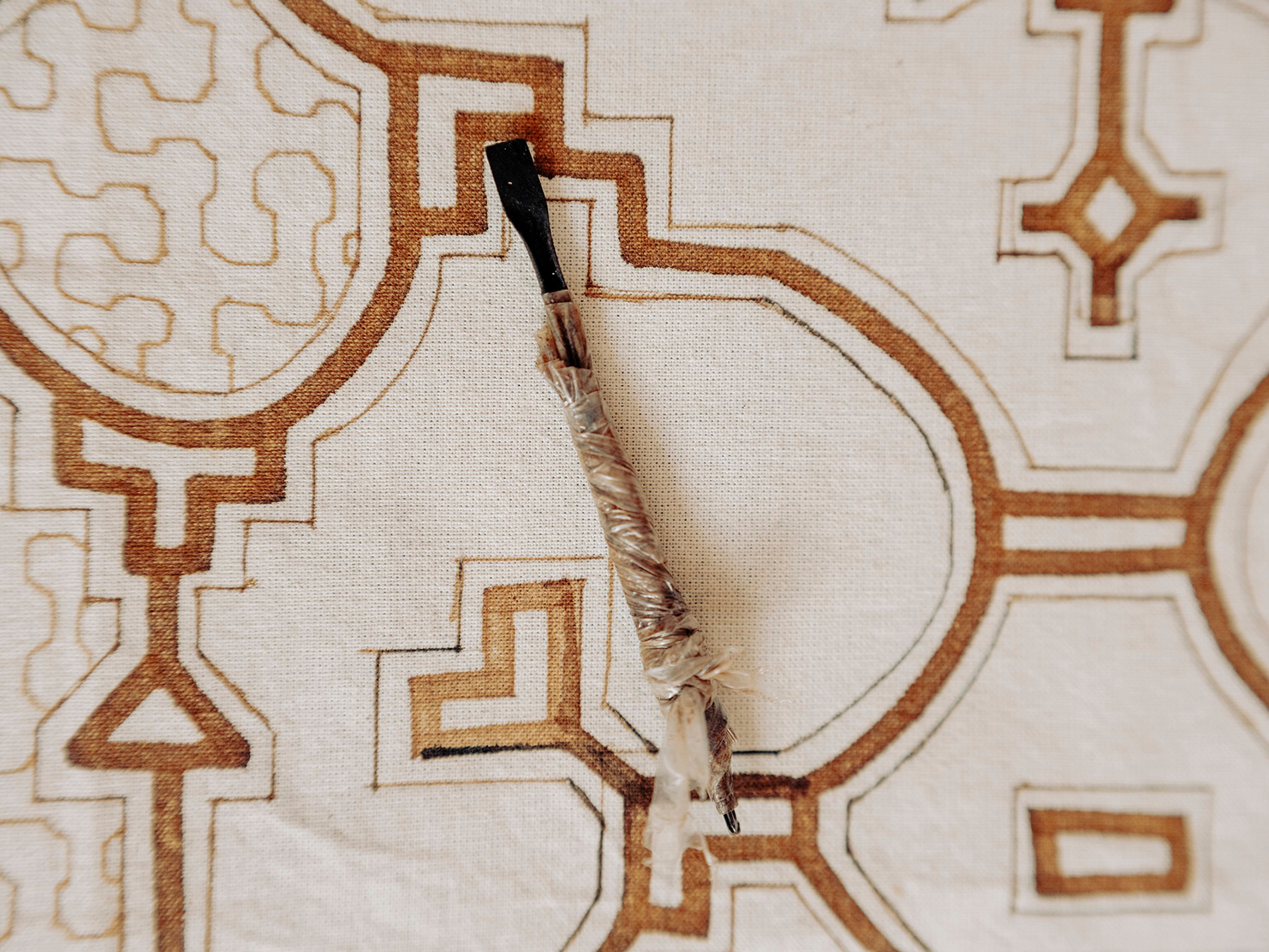 A brush rests on a light fabric with intricate brown geometric patterns.