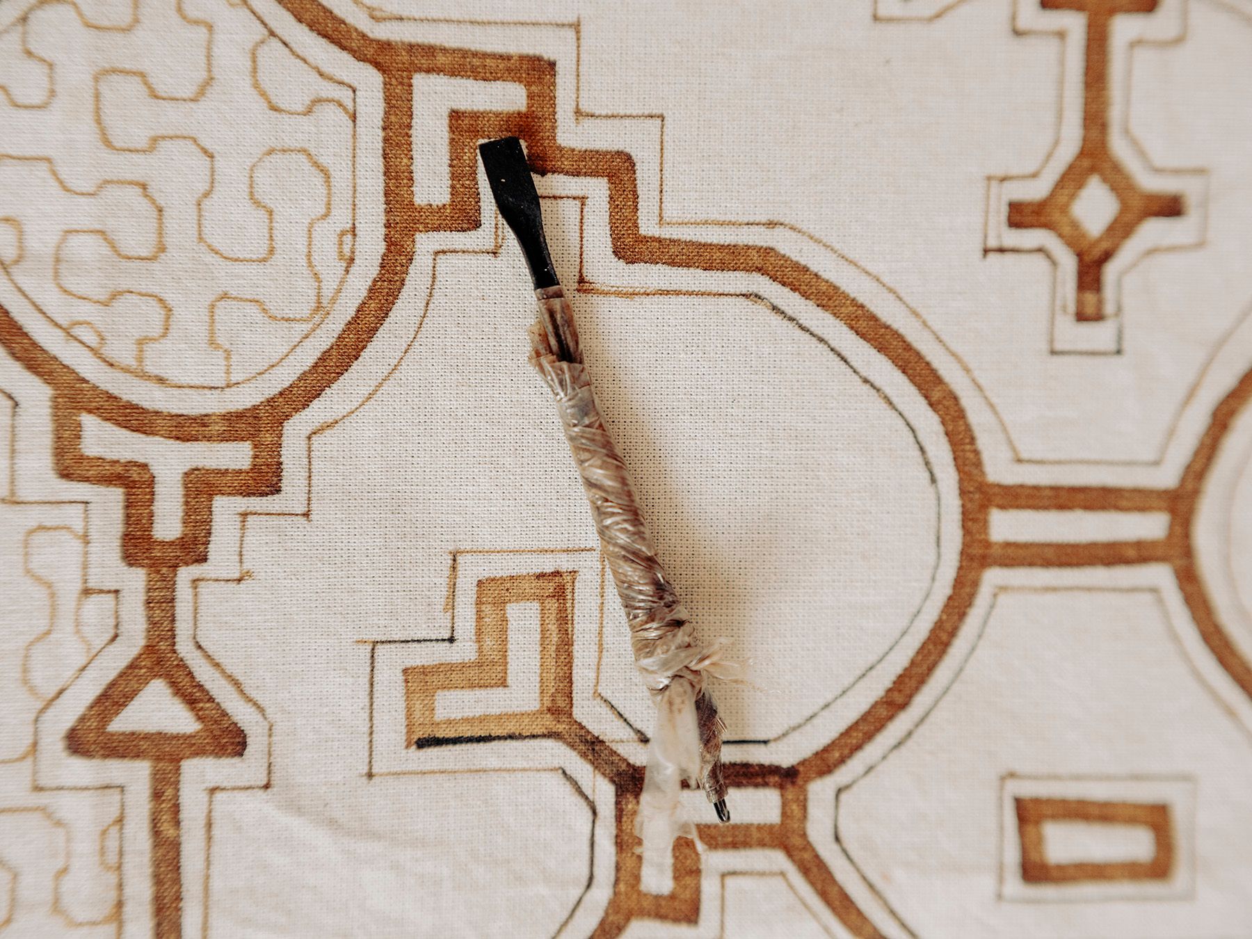 A brush rests on a light fabric with intricate brown geometric patterns.