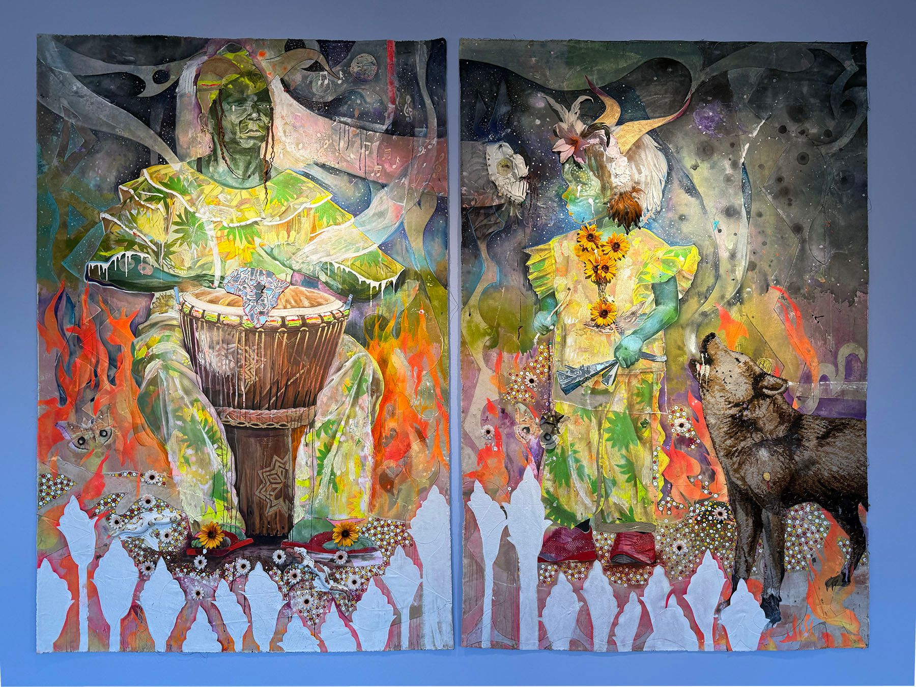 A vibrant diptych painting shows two green-skinned figures in patterned yellow-green clothing. The left figure plays a drum surrounded by orange flames; the right figure, with a horned headdress and sunflowers, stands by a howling wolf against a dark, swirling background.