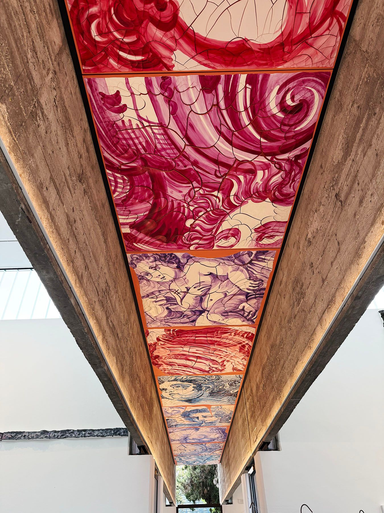 Long underside of a structure with painted panels in red, pink, purple, and blue abstract and figurative designs, between concrete beams.