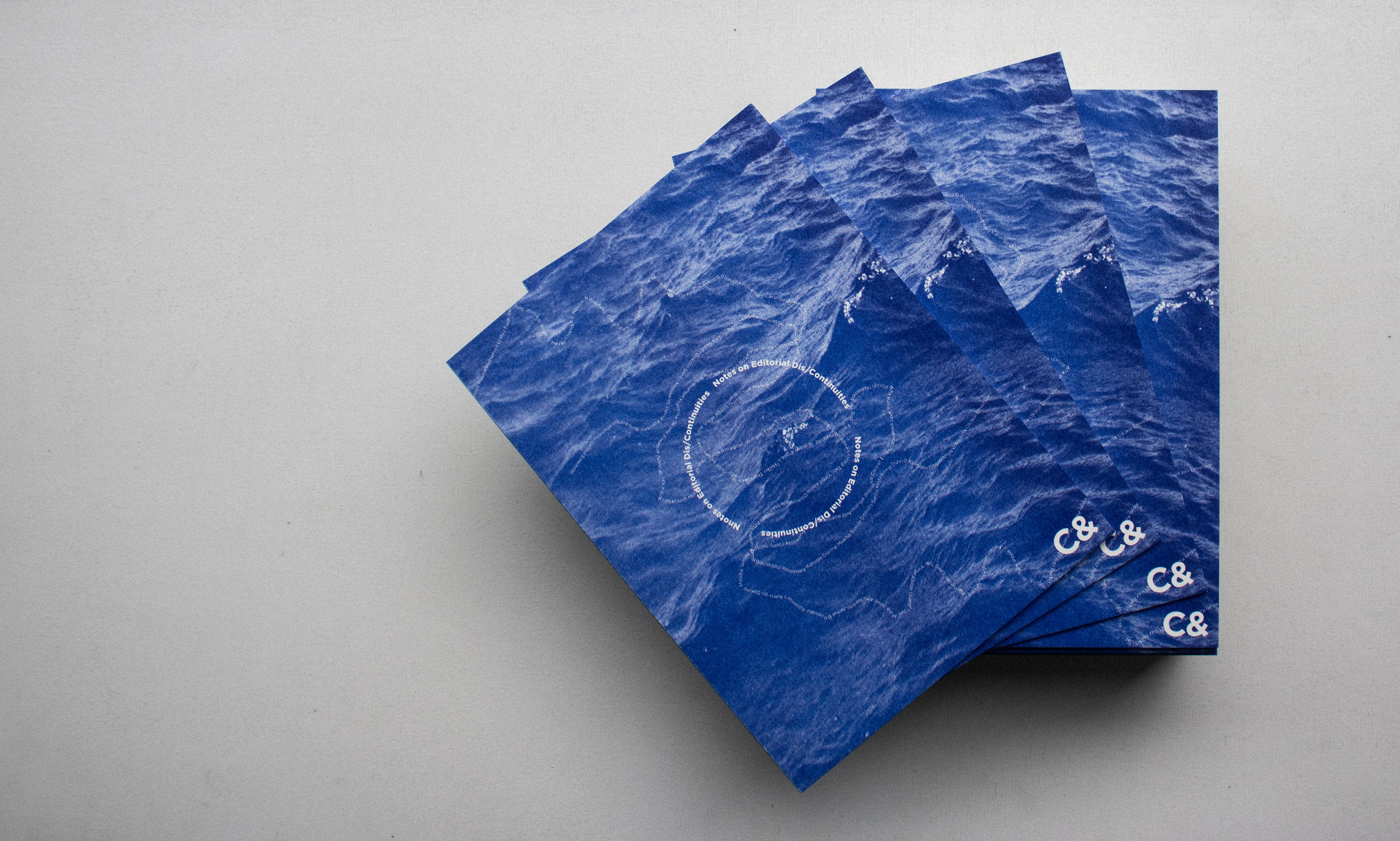 A stack of blue publications with an ocean wave design, a white circular pattern, and "C&" logo.