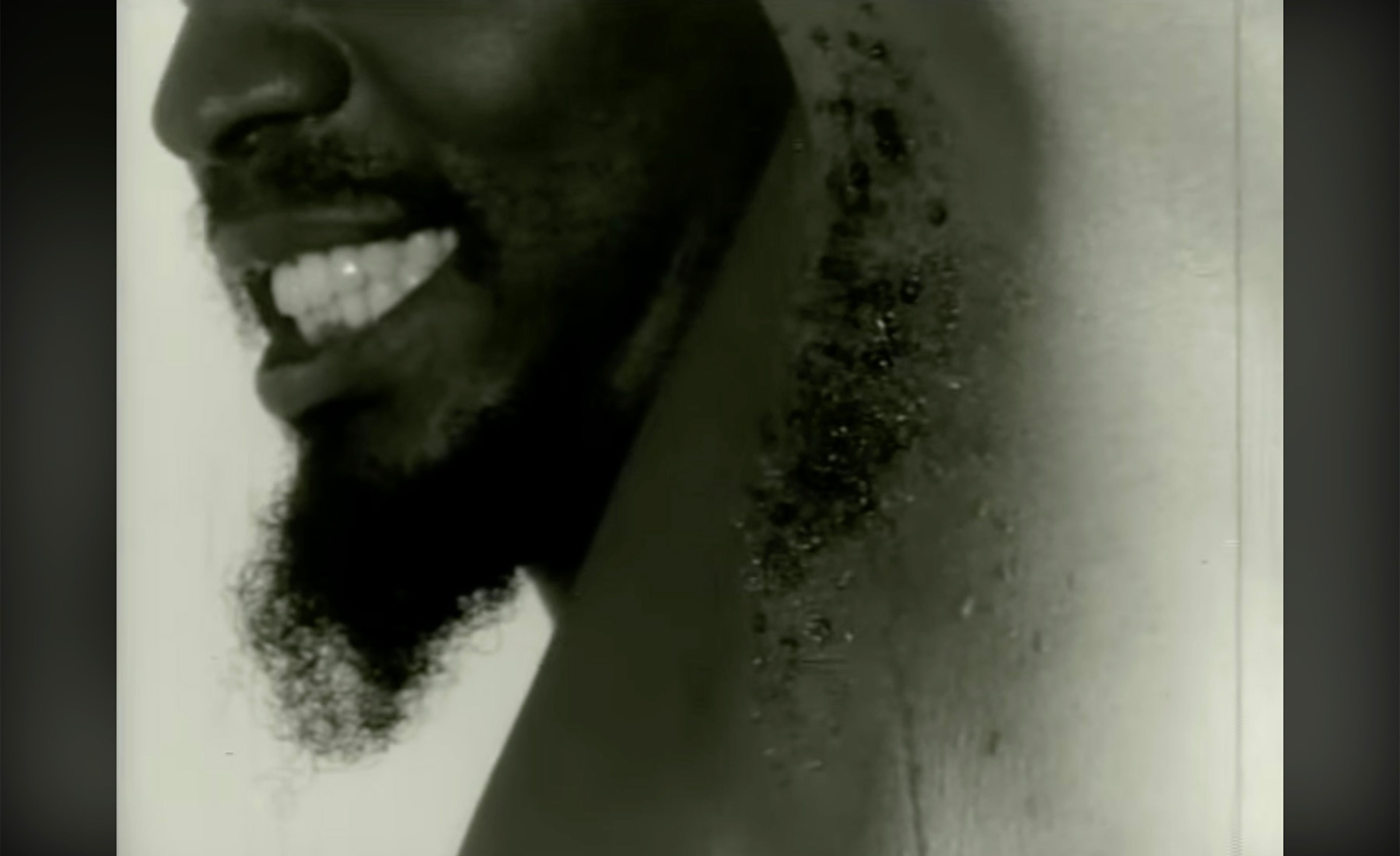 Black and white profile of a smiling man with a beard and a wet armpit.