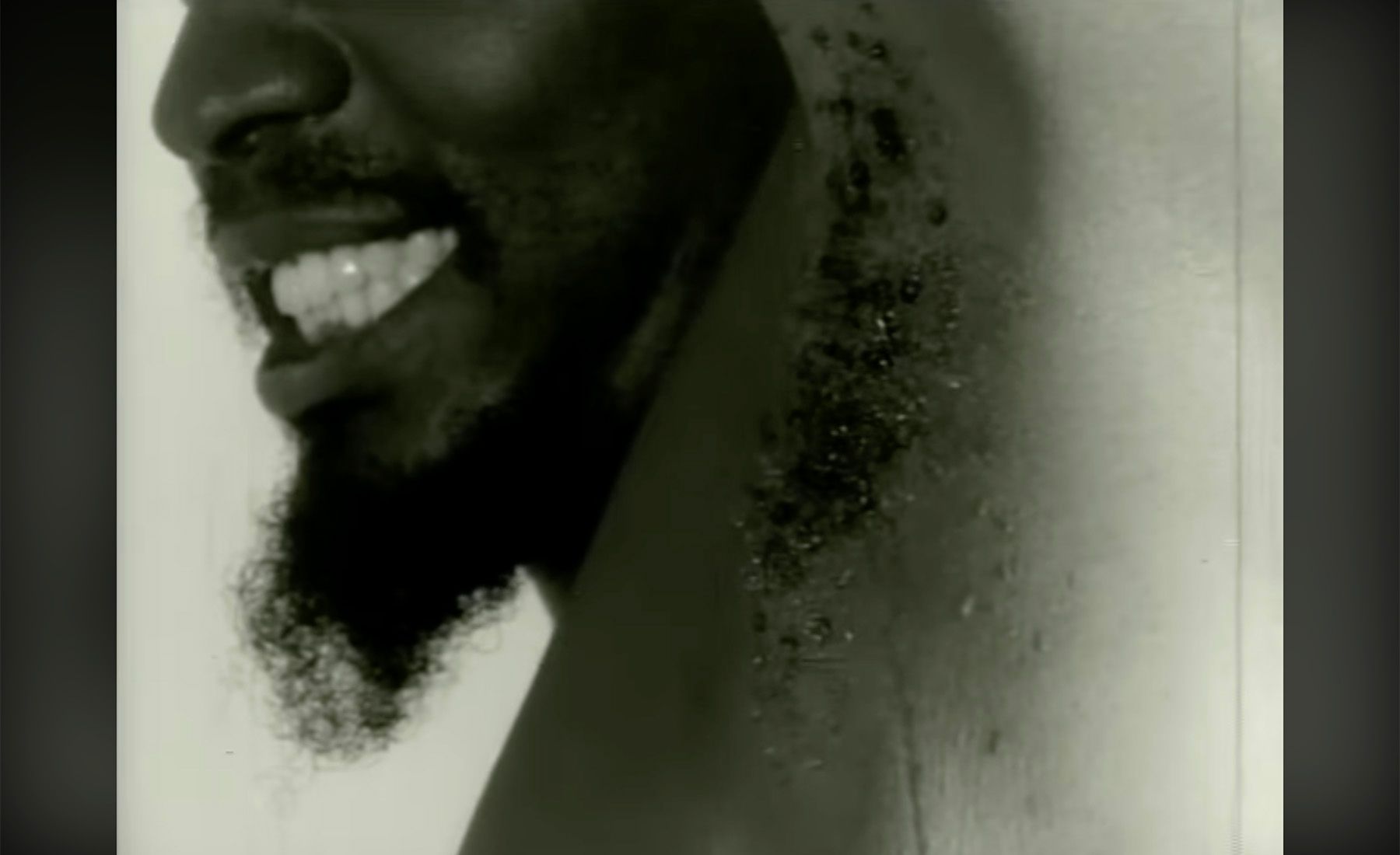 Black and white profile of a smiling man with a beard and a wet armpit.