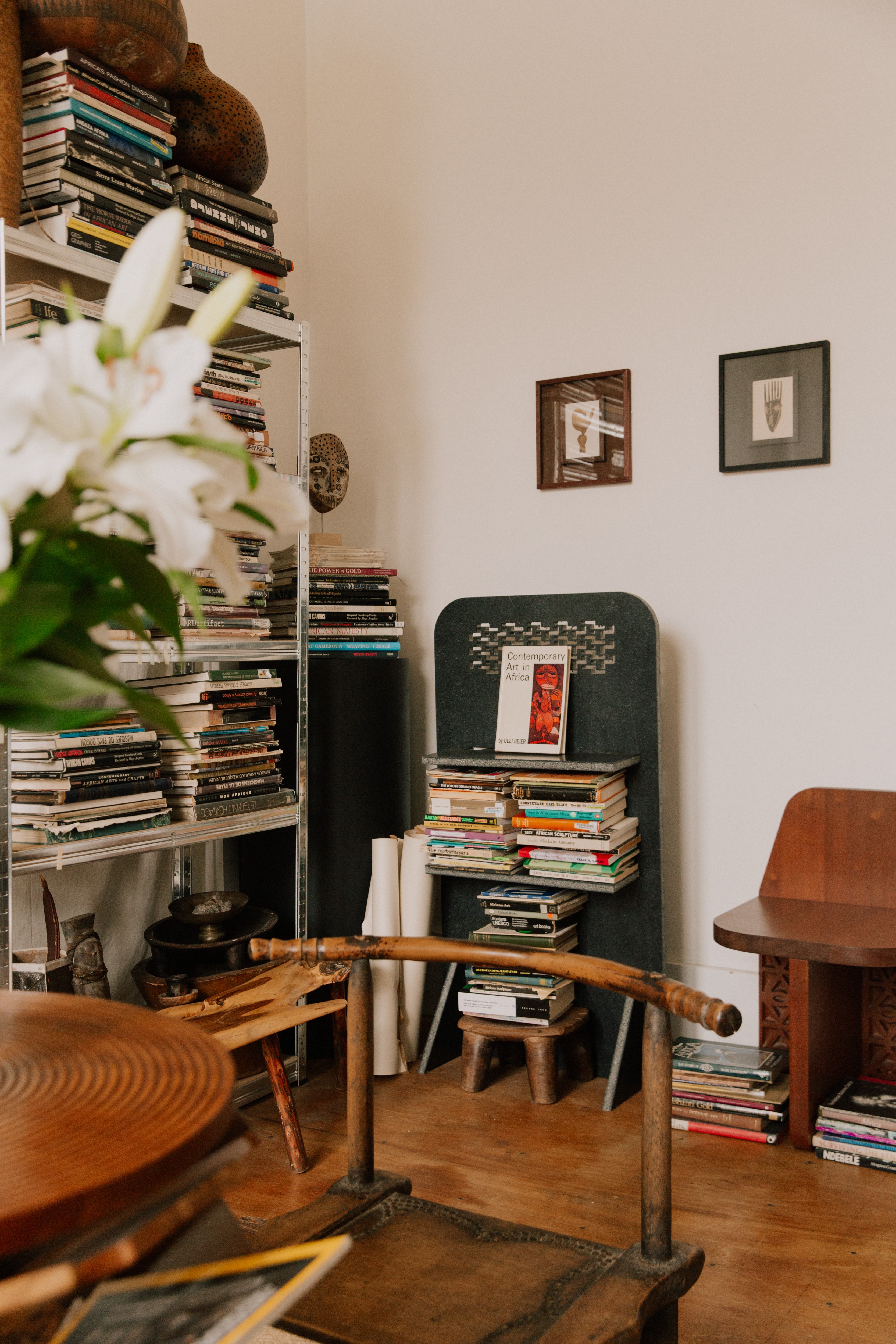 A room filled with books on shelves, various art objects, and white lilies in the foreground.