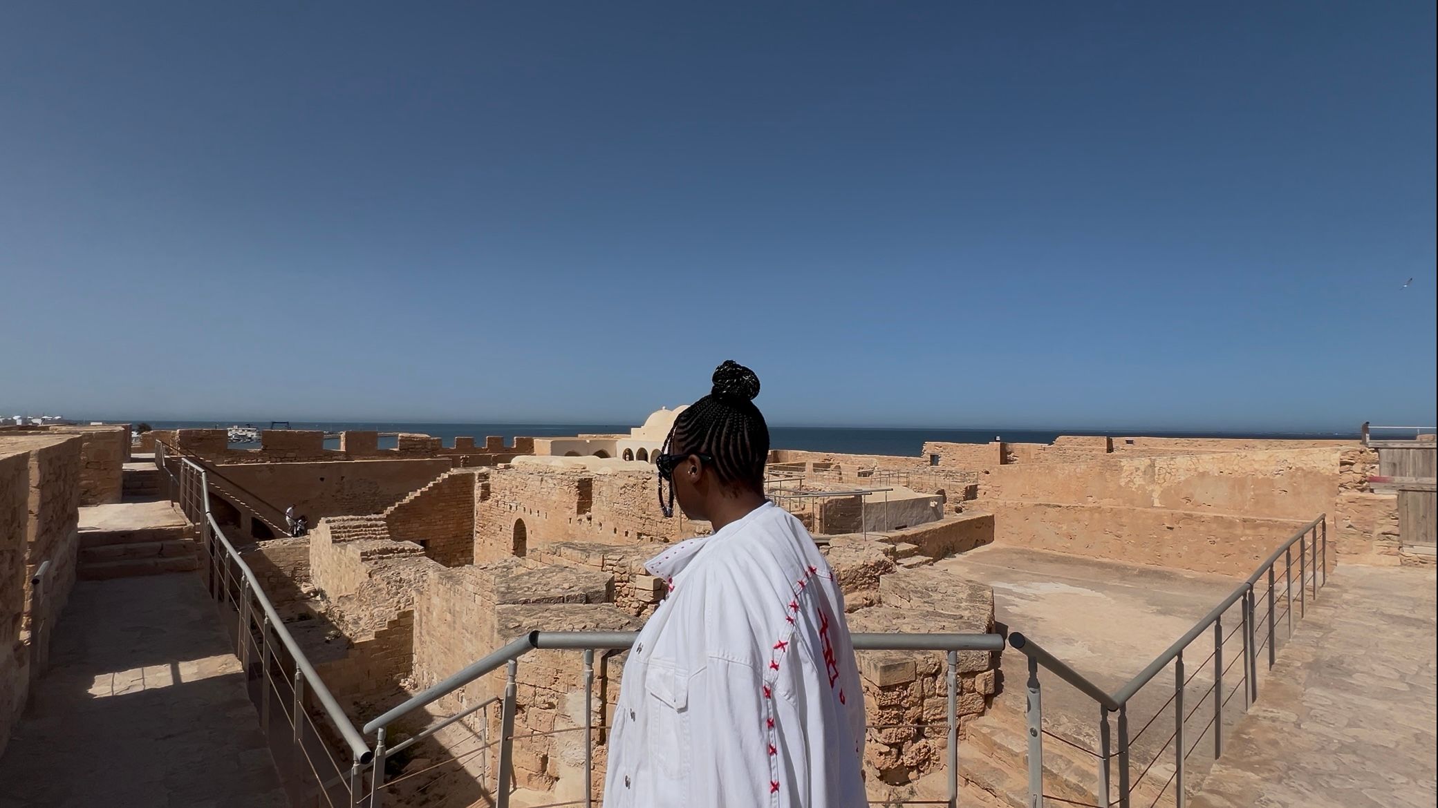 Woman looking over ancient stone ruins toward the sea.