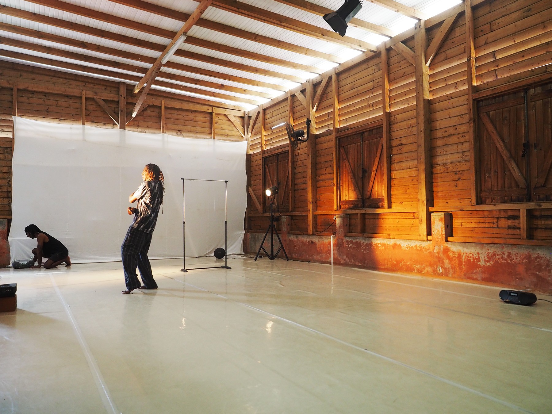 Two people on a set in a rustic wooden studio with a white backdrop.
