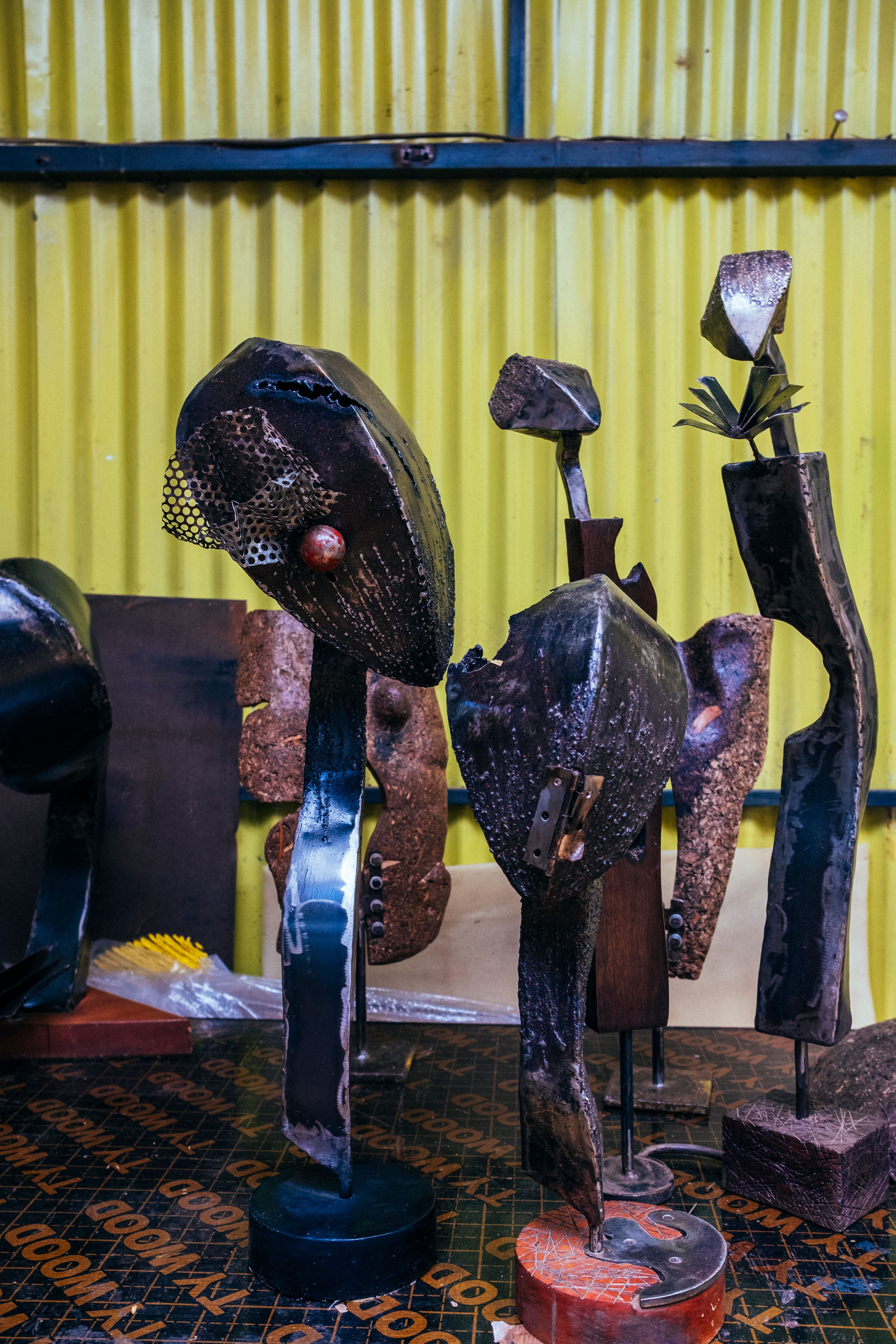 Abstract dark metal sculptures of figures displayed against a yellow wall.