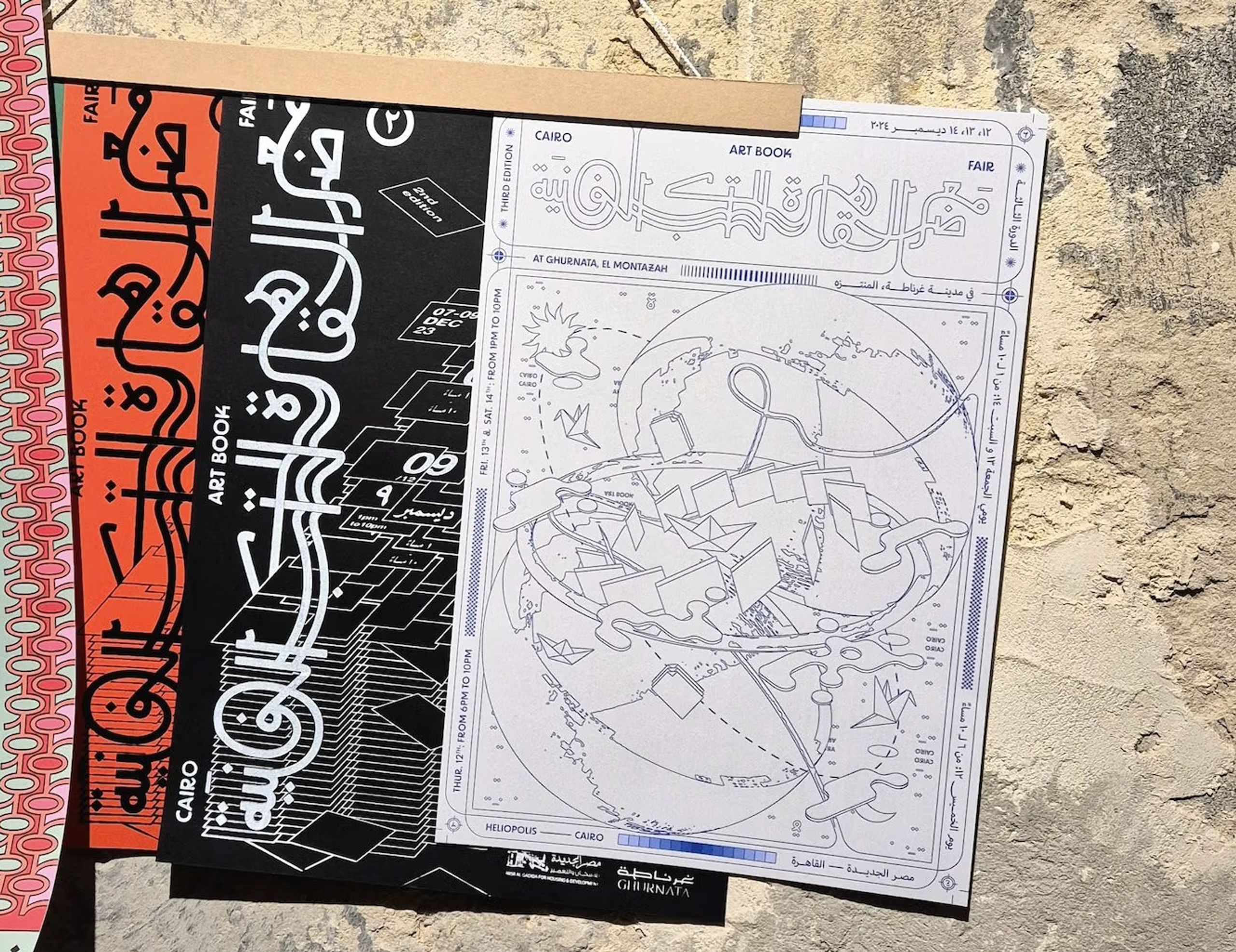 A fanned display of art books with Arabic script and graphic designs, on a rough concrete surface.