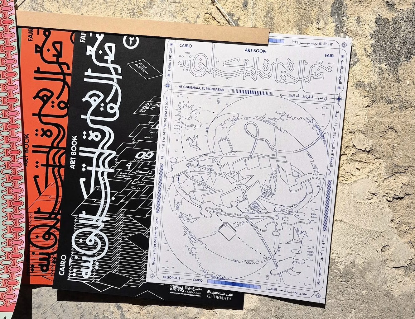 A fanned display of art books with Arabic script and graphic designs, on a rough concrete surface.