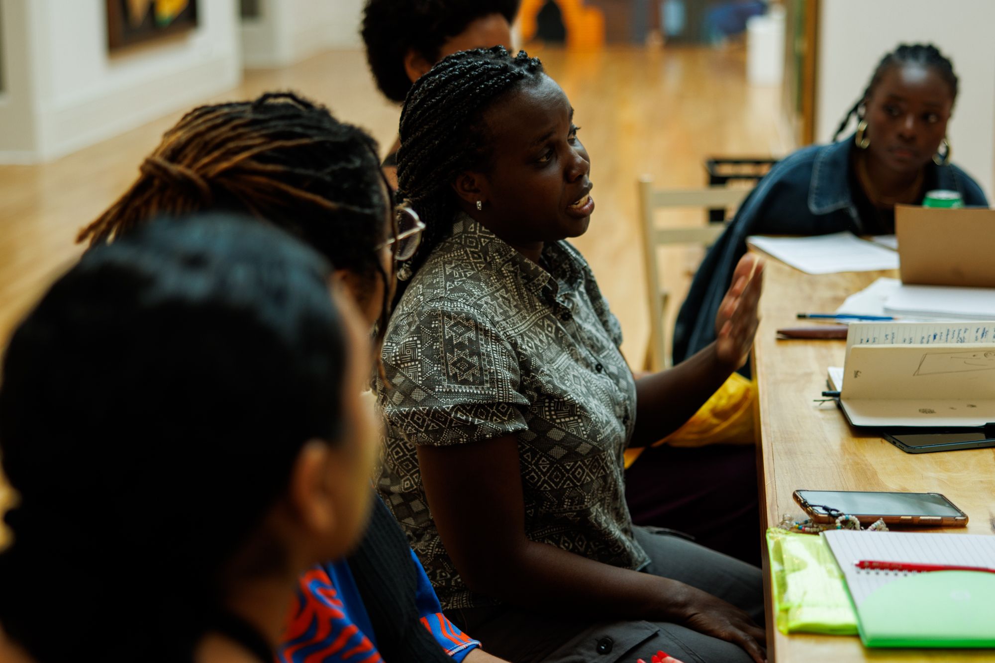 A Black woman speaks and gestures with her hand at a wooden table during a group discussion.
