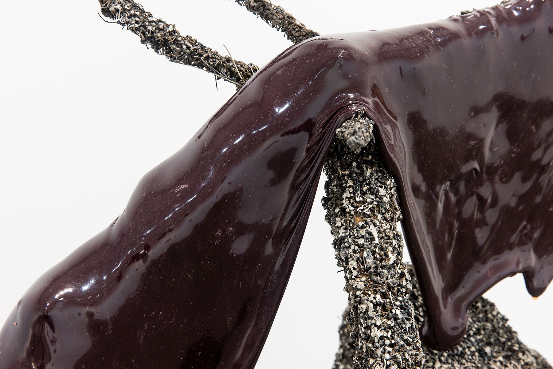 Dark, glossy plum-colored substance draped over a textured, granular grey sculpture.