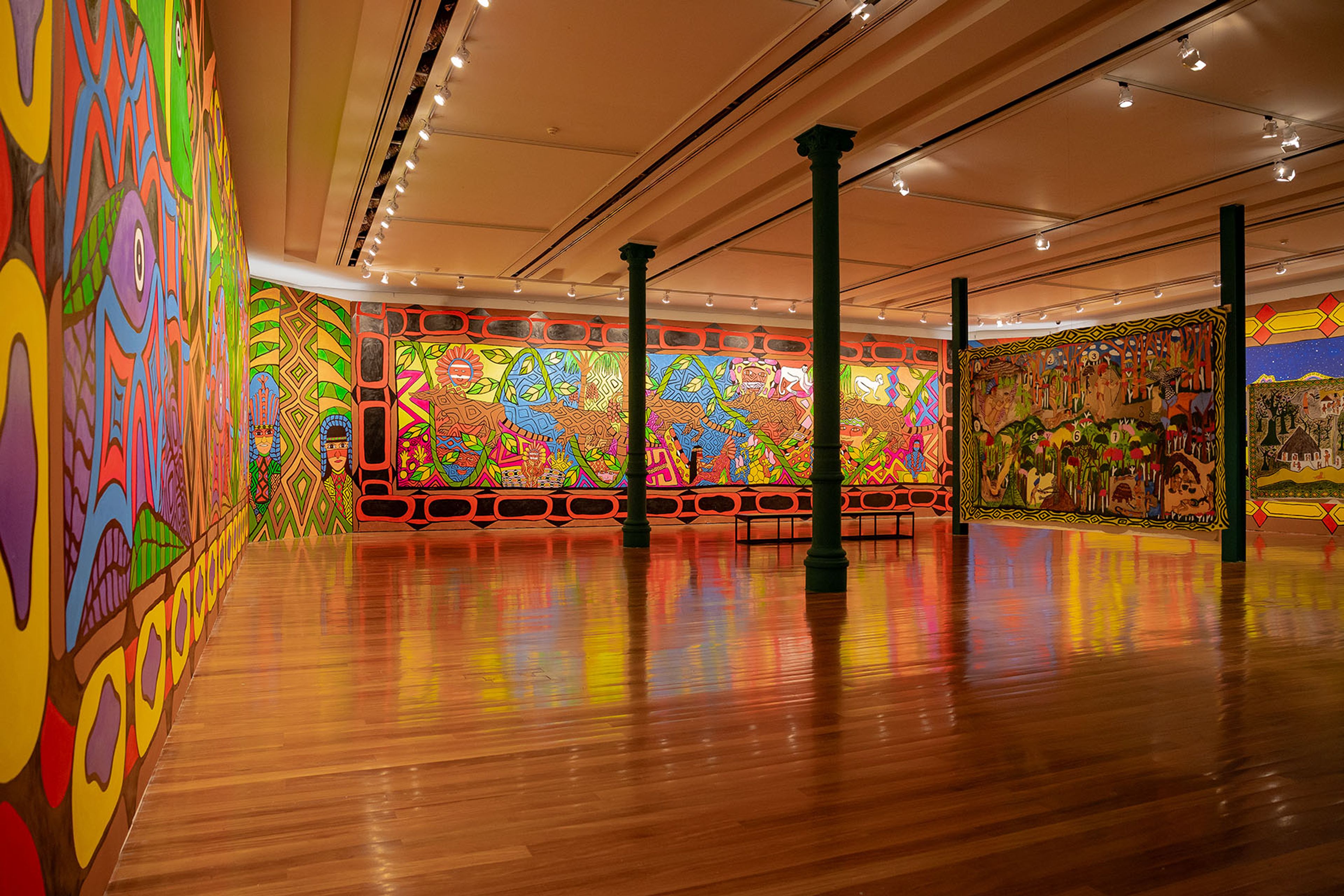 A vibrant art gallery features colorful murals and large tapestries on walls, with a polished wooden floor and dark green pillars.
