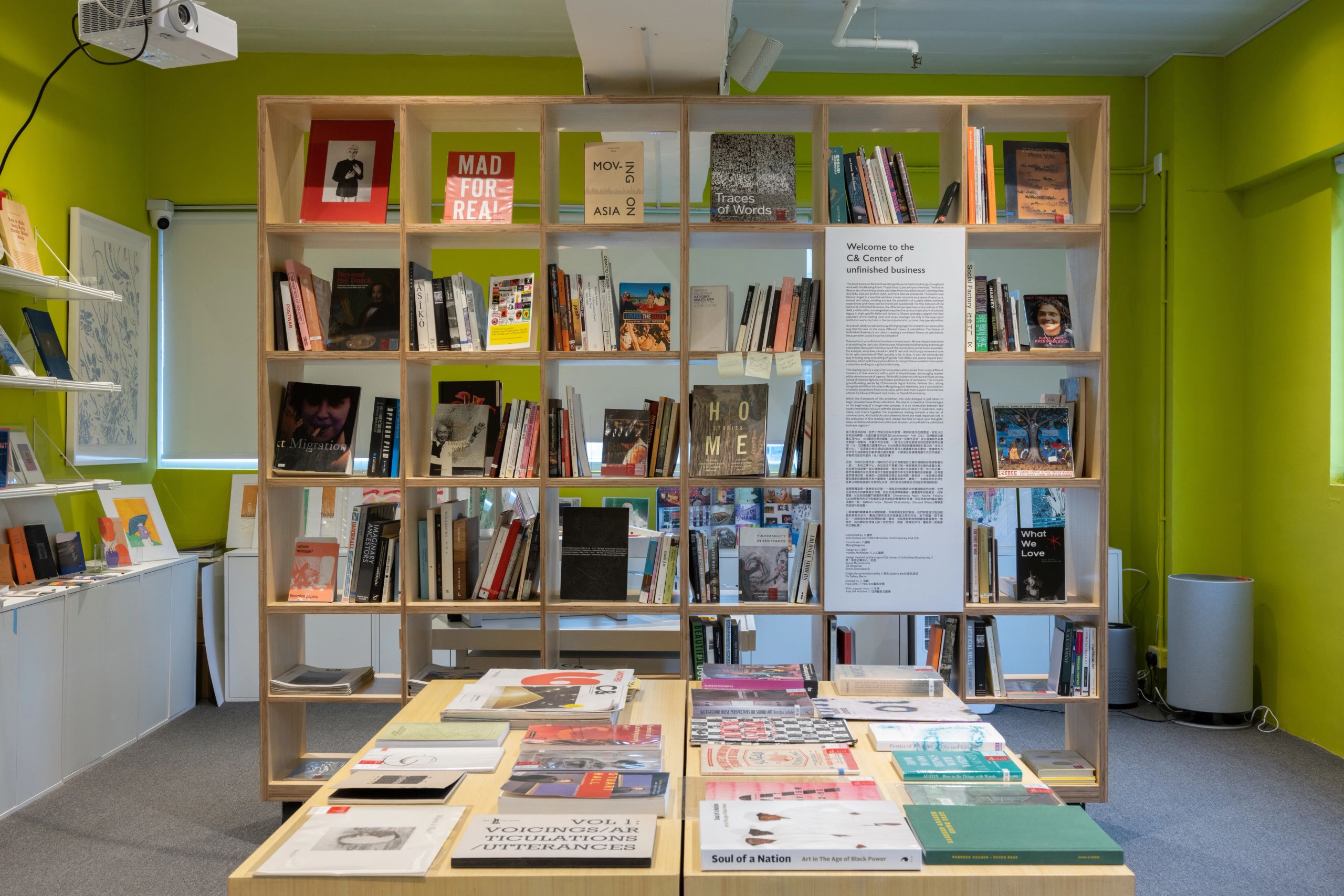 A room with lime green walls, featuring a large wooden bookshelf full of books, and a table displaying more books in the foreground.