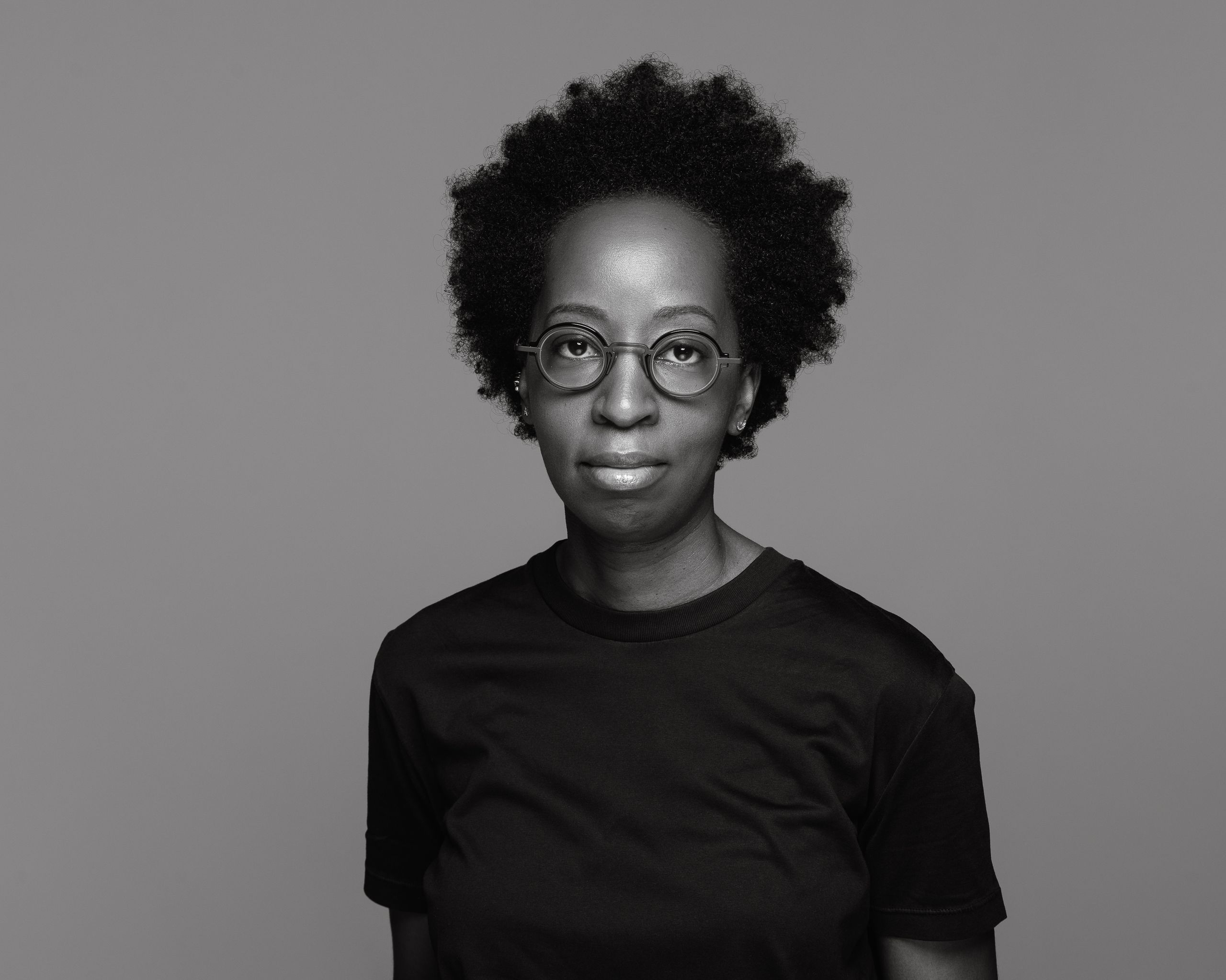 Black and white photo of a Black woman with curly hair and round glasses.